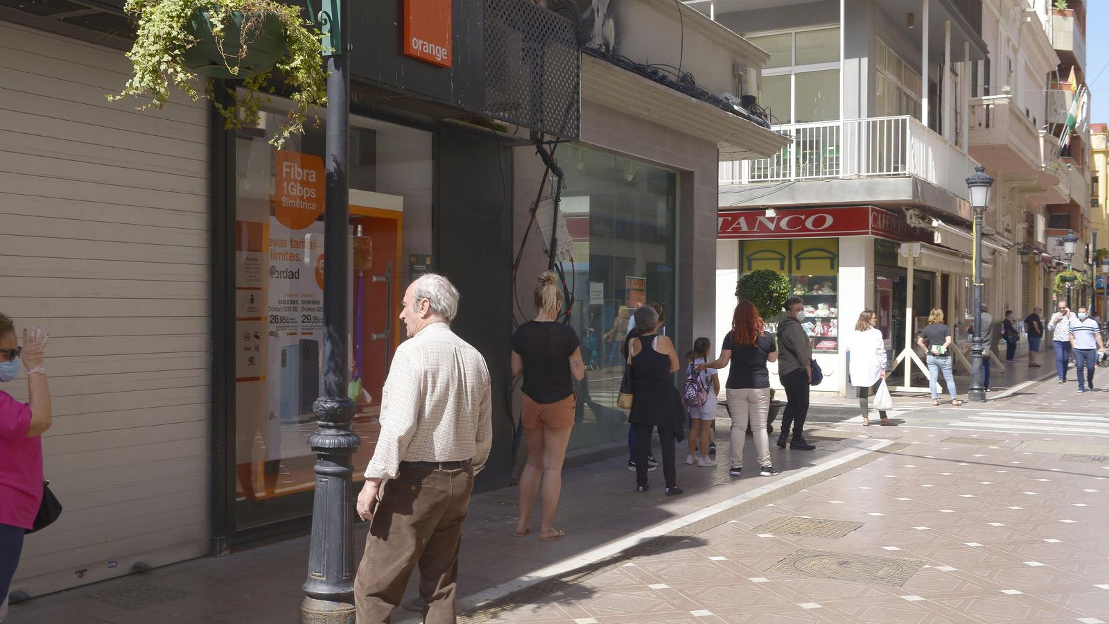 Una hilera de clientes guarda turno para entrar a comprar pan mientras la cola alcanza una tienda cerrada.