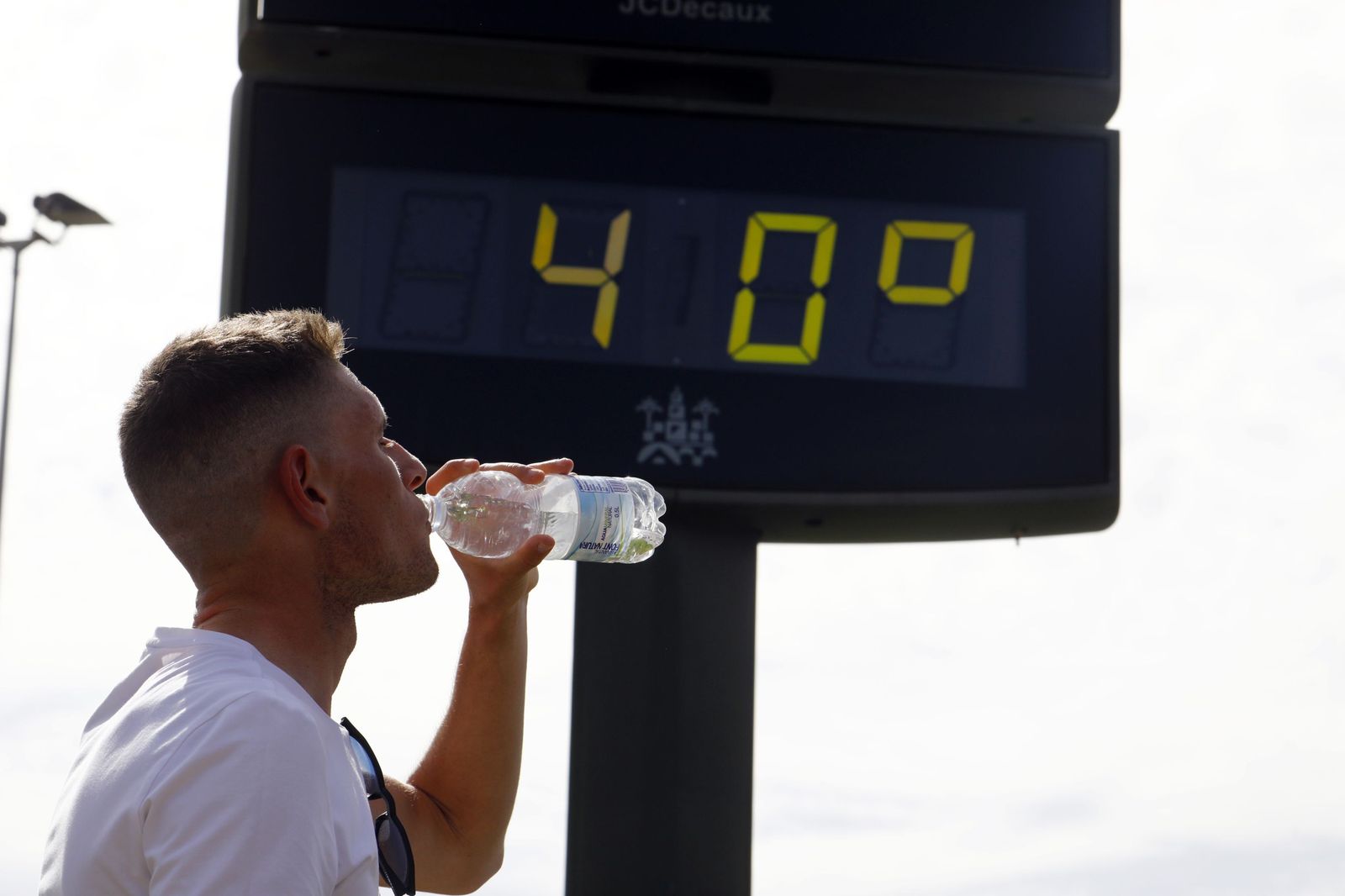 Un hombre bebe agua de una botella delante de un termómetro con 40 grados.