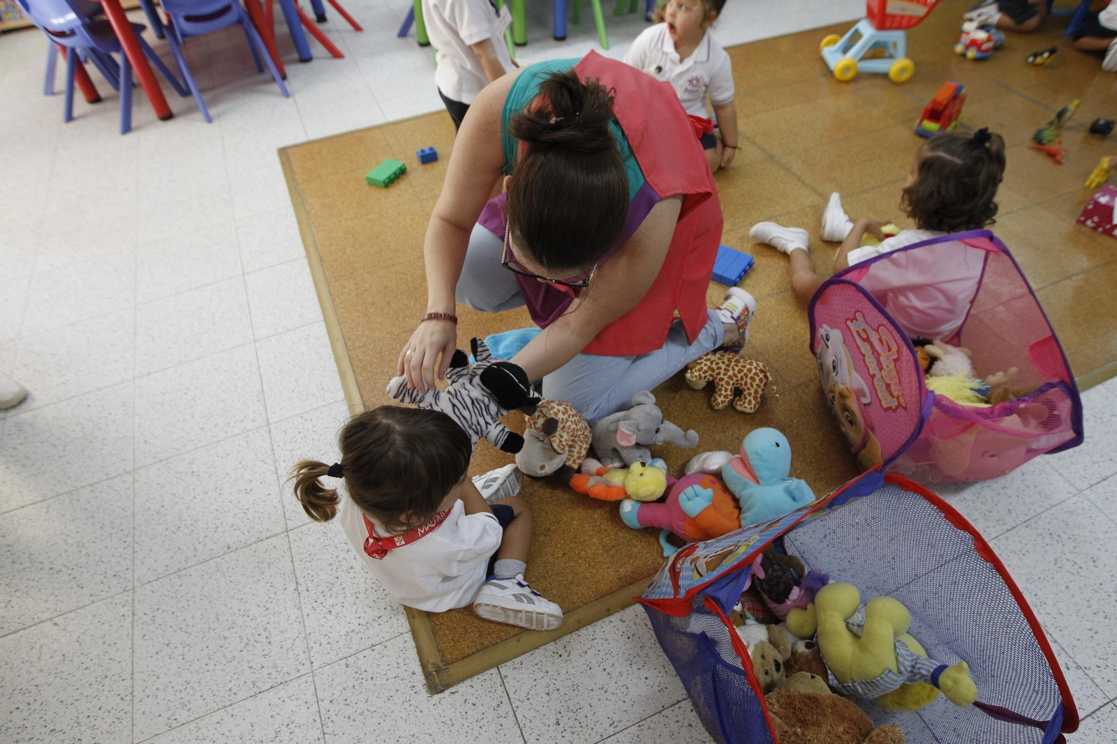 Una maestra atiende a una niña en una escuela infantil.