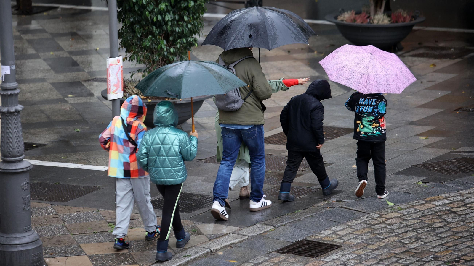 Varias personas pasean con paragüas por la ciudad. Varias personas pasean con paragüas por la ciudad.