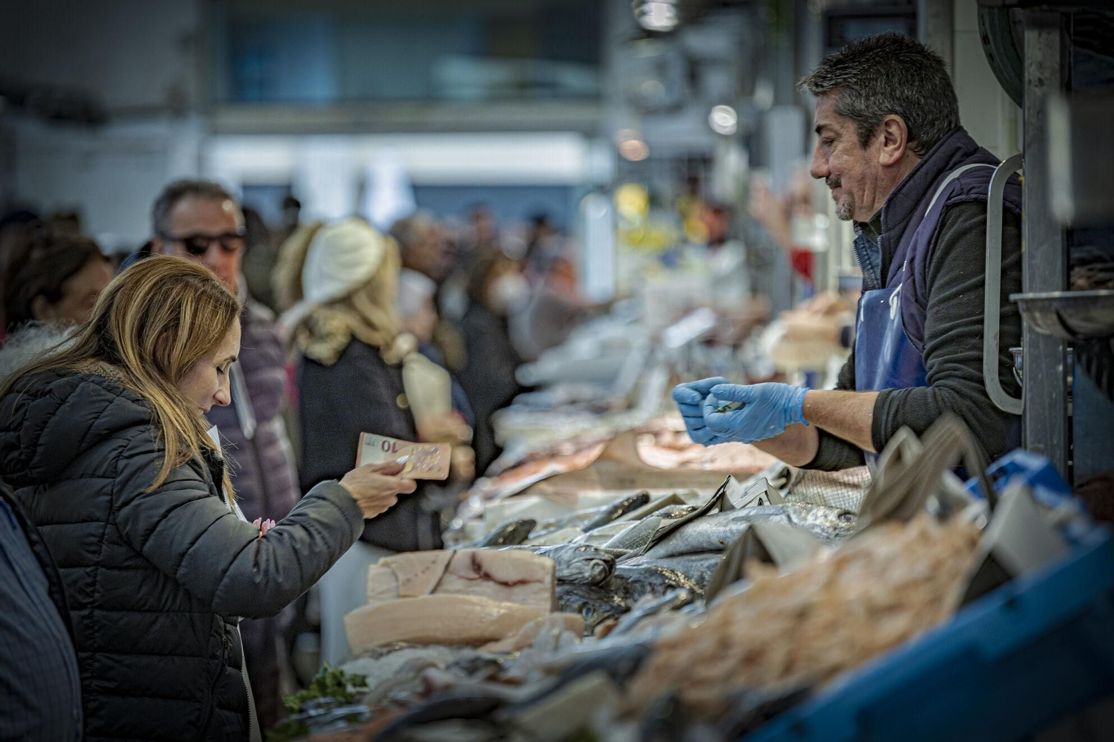 Una mujer paga en efectivo al tendero de una pescadería en un mercado
