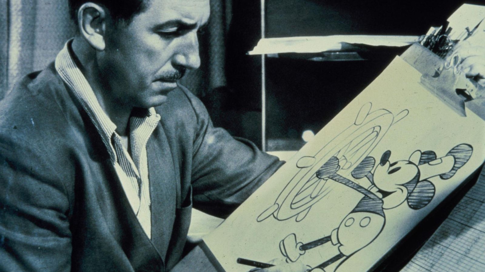 Walt  Disney  aparece en la mesa de dibujo con un boceto de su famoso personaje Mickey.