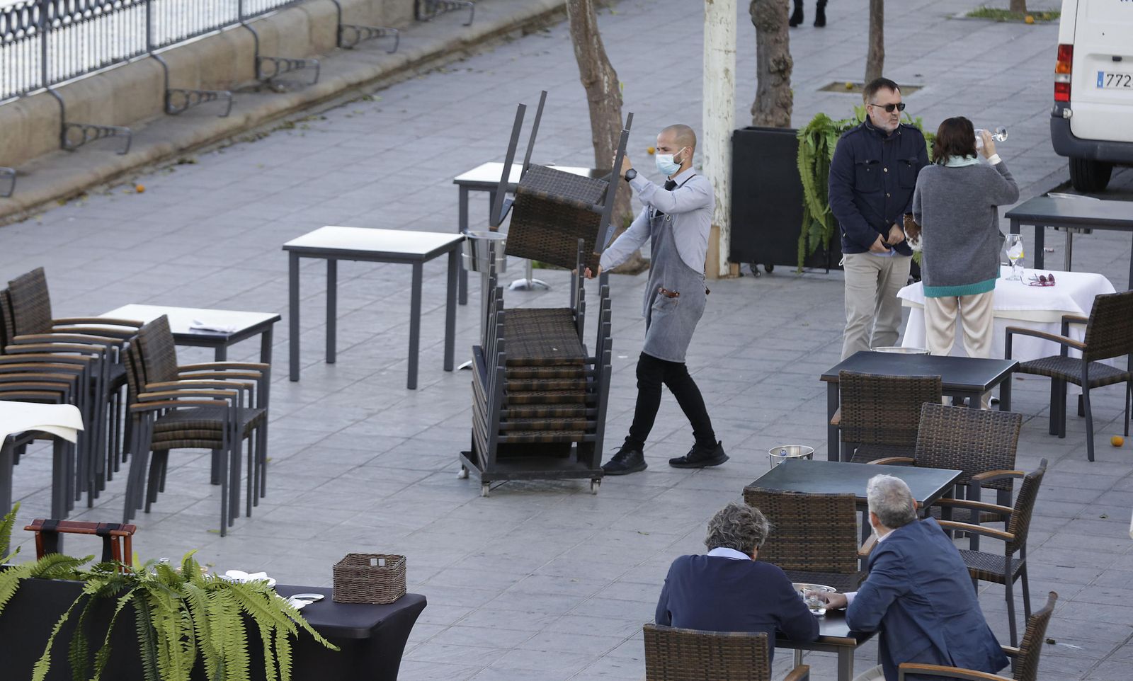 Un camarero recoge las sillas del velador de un restaurante en la calle Betis.