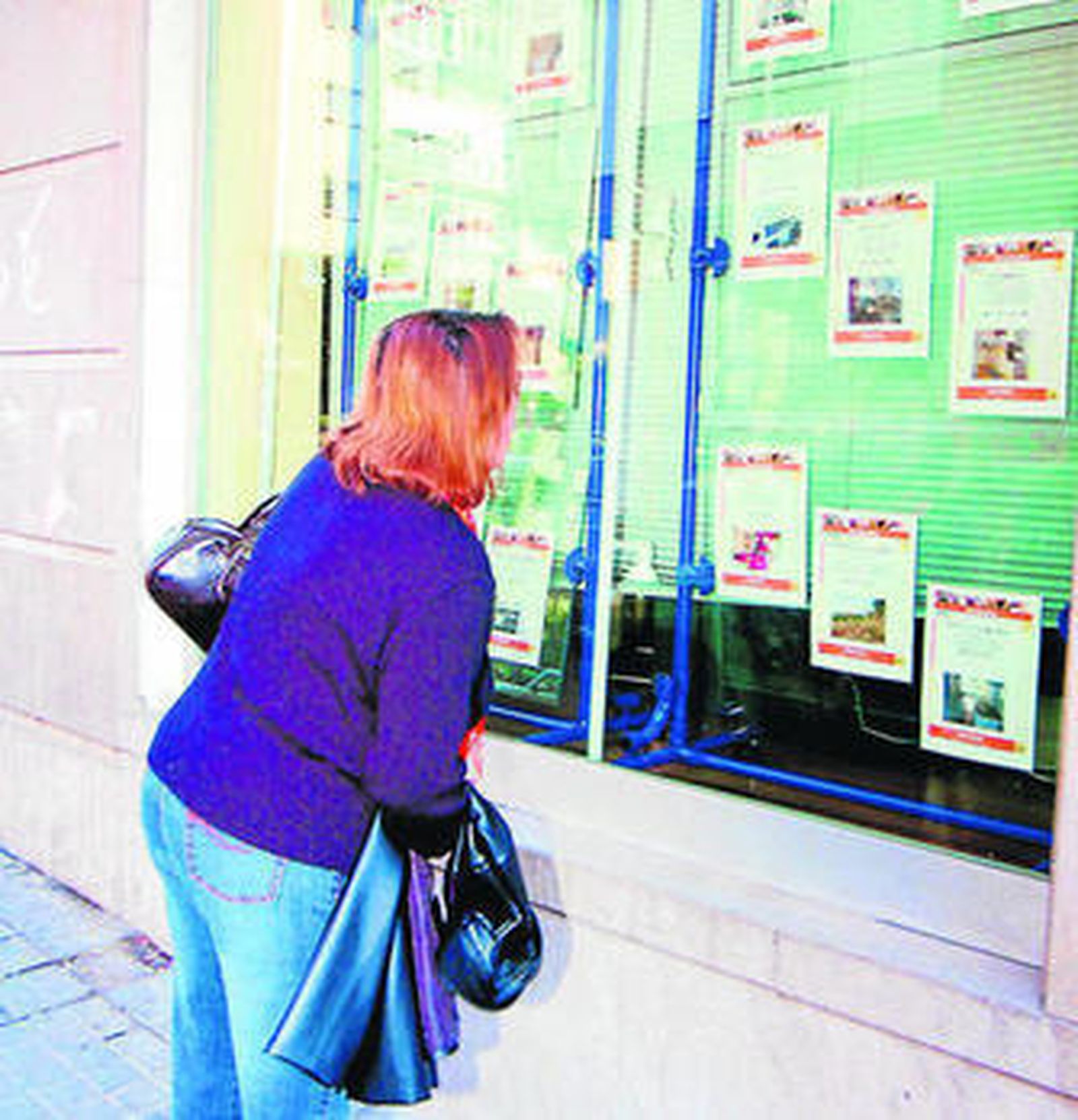 Una señora observa el escaparate de una inmobiliaria.