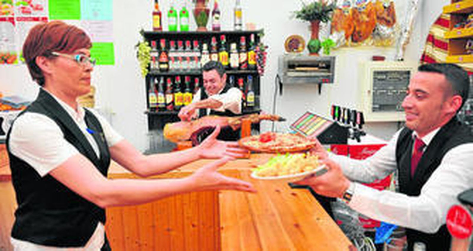 Camareros de una caseta de la calle Juan Belmonte sirven langostinos y pescado frito, mientras otro corta jamón al fondo.
