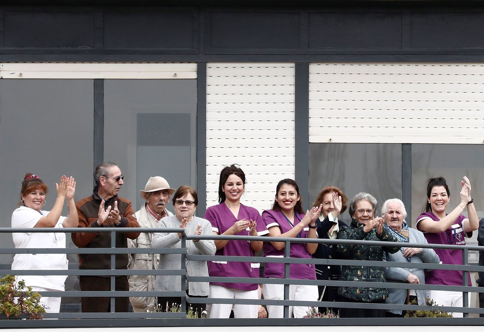 Varios abuelos y sus cuidadoras aplauden desde el balcón de la residencia en la que viven.