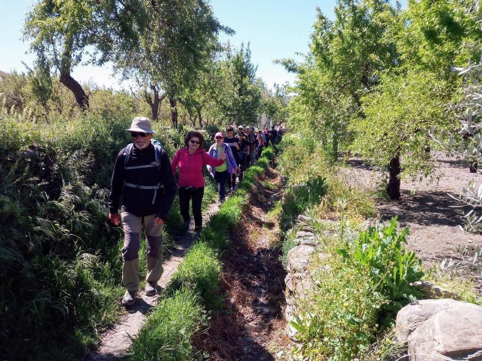 Los participantes caminan junto a una acequia, en mitad de un paisaje muy bonito.