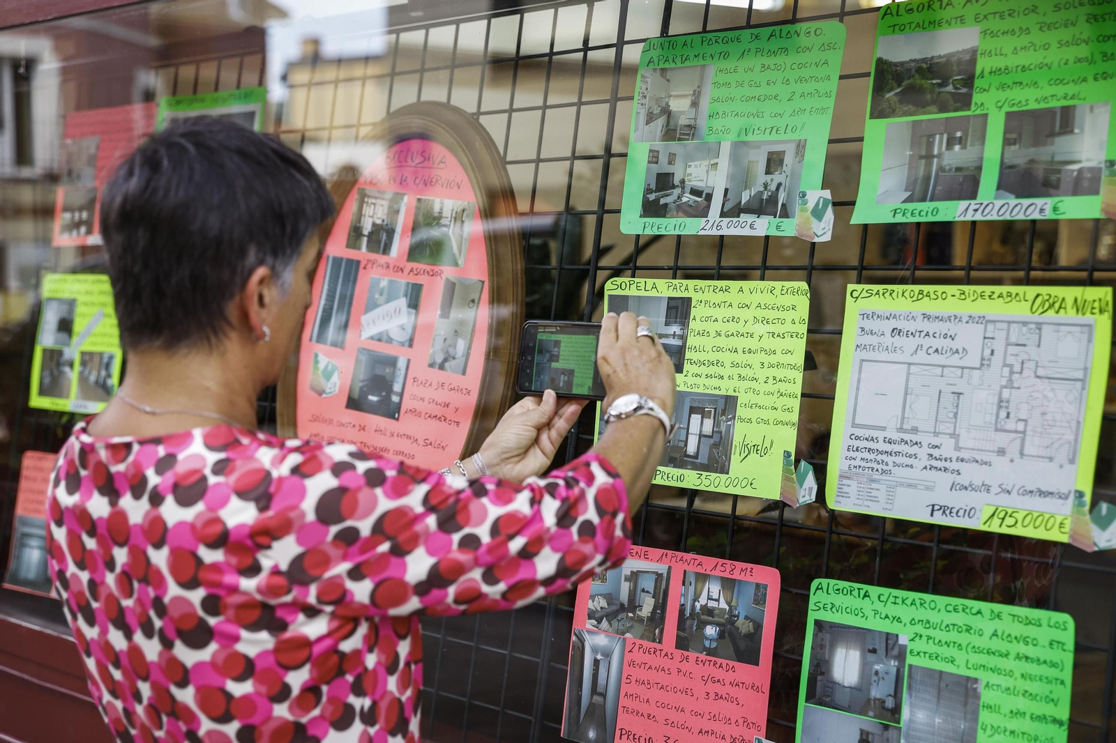 Una mujer pega anuncios de venta de viviendas en la fachada de una inmobiliaria.