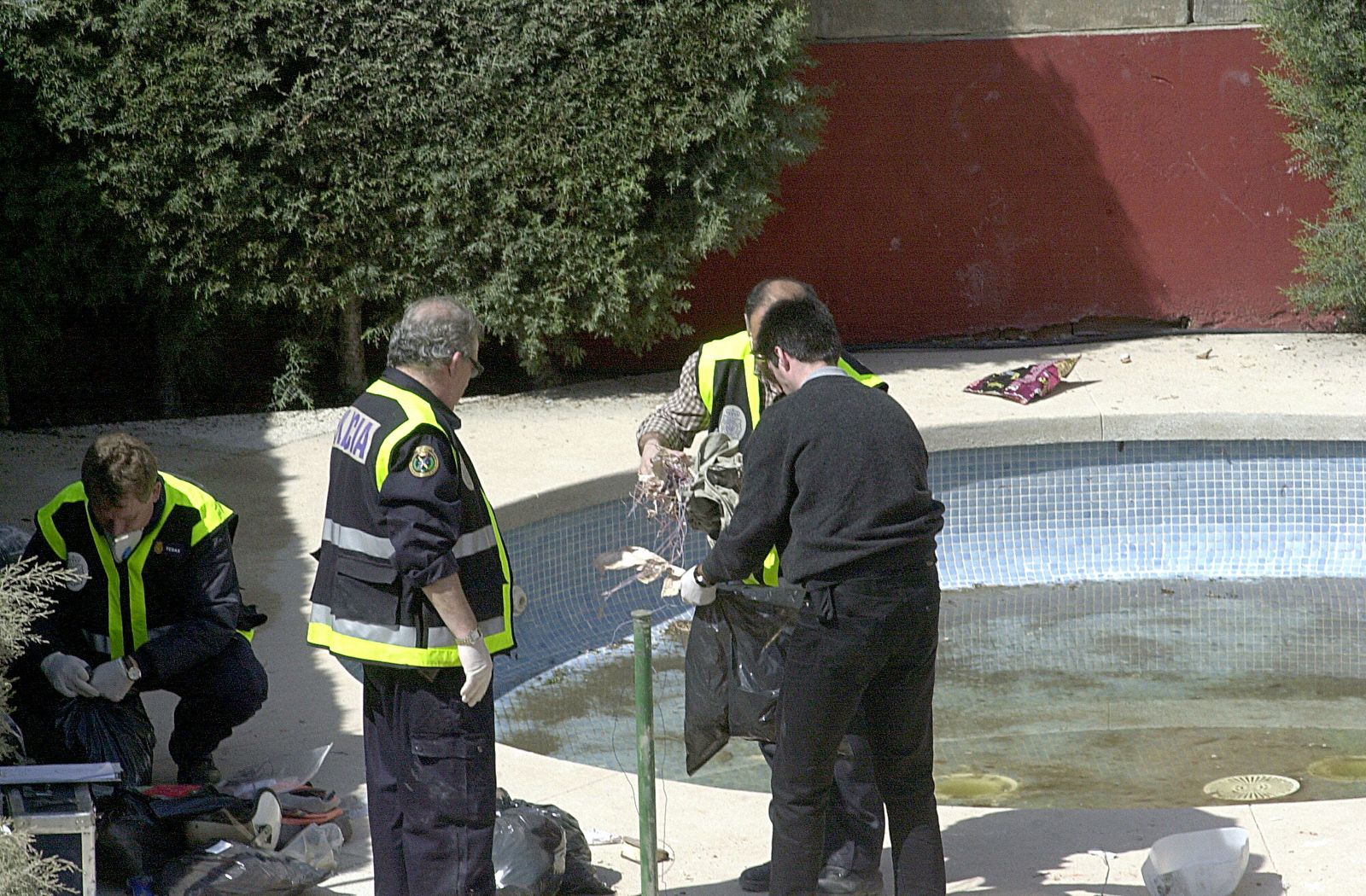 Varios agentes de policía trabajando en un caso junto a una piscina.