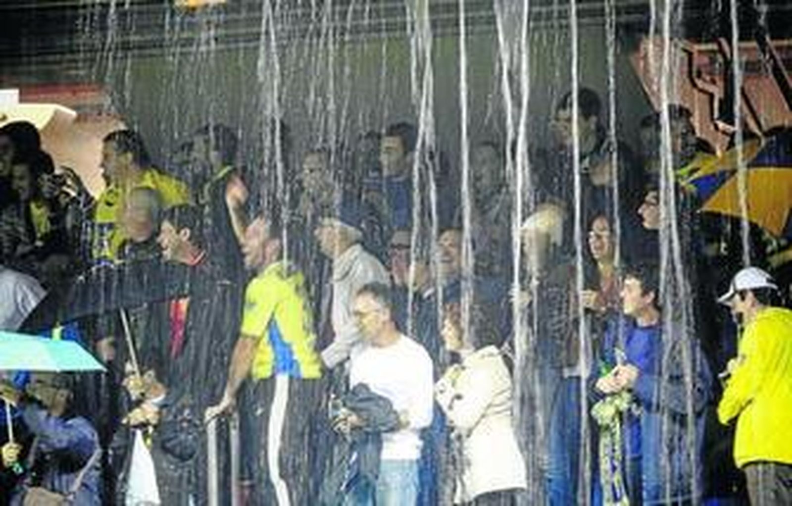 Un grupo de seguidores se protege de la lluvia mientras sigue con atención el partido.