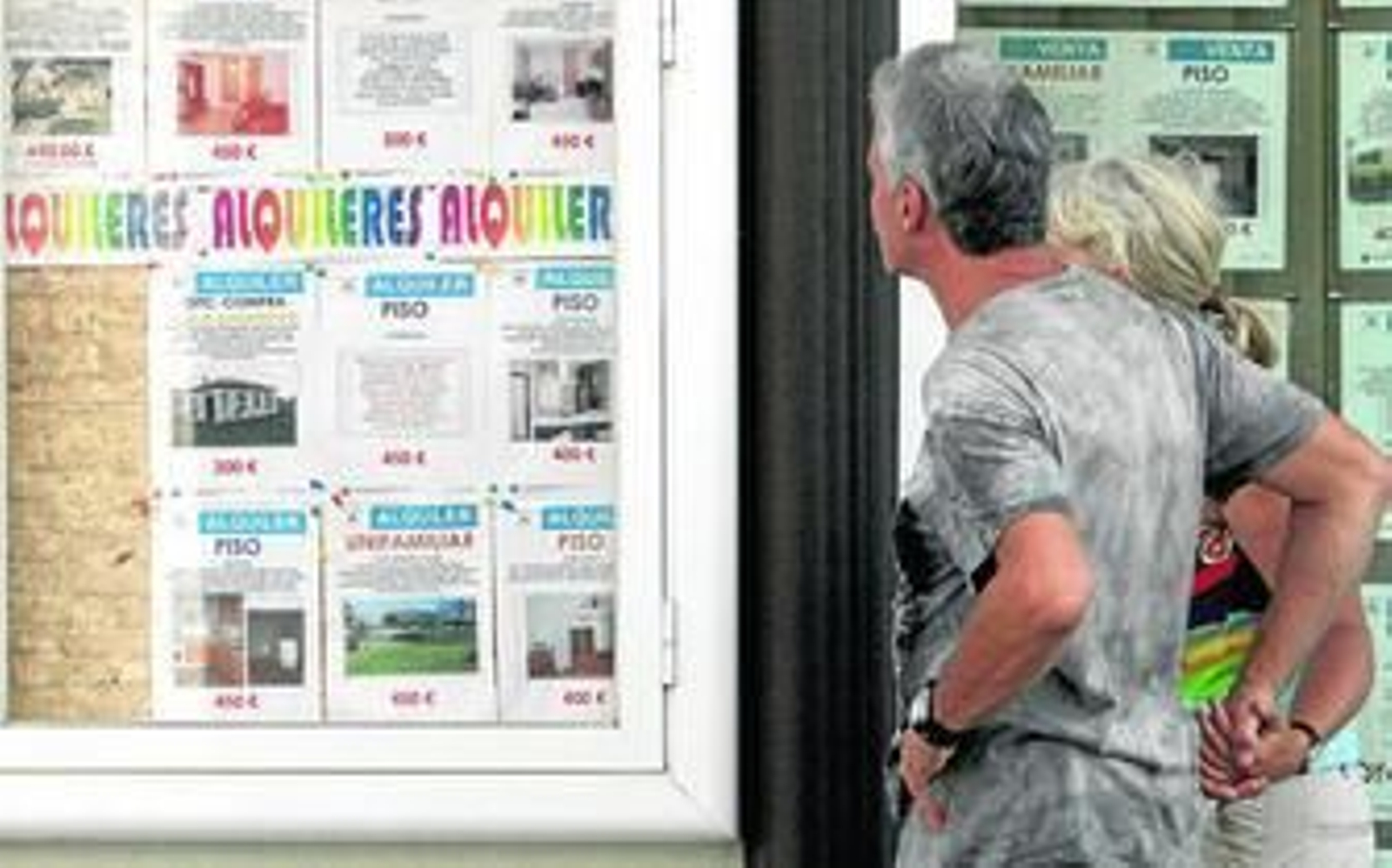 Una pareja observa carteles de alquileres de pisos en una inmobiliaria.