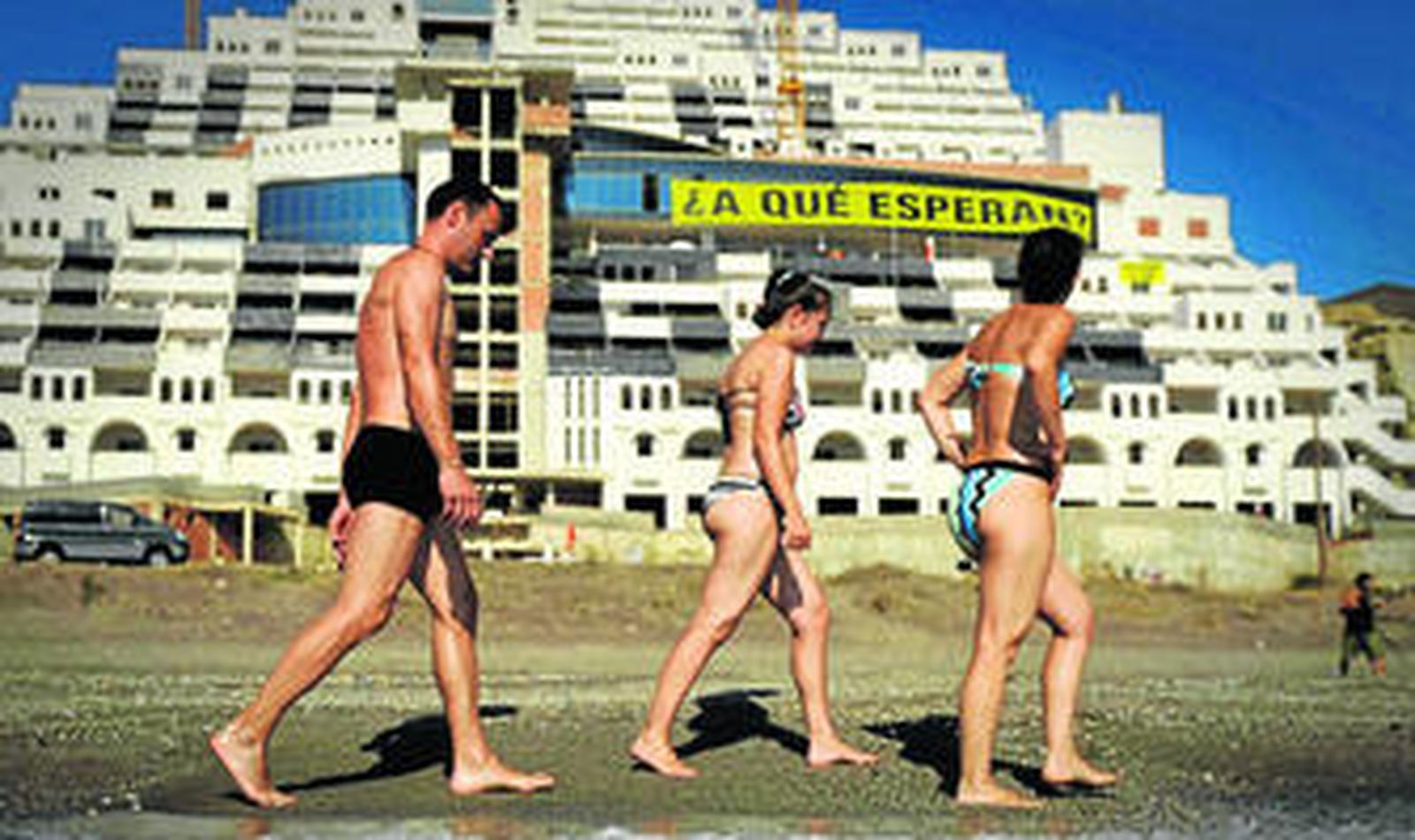 Unos bañistas pasan ante la construcción paralizada del hotel, en la playa del Algarrobico.