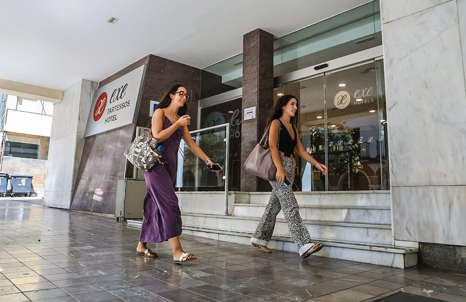 Dos jóvenes caminan frente a uno de los hoteles de Huelva capital, este martes.