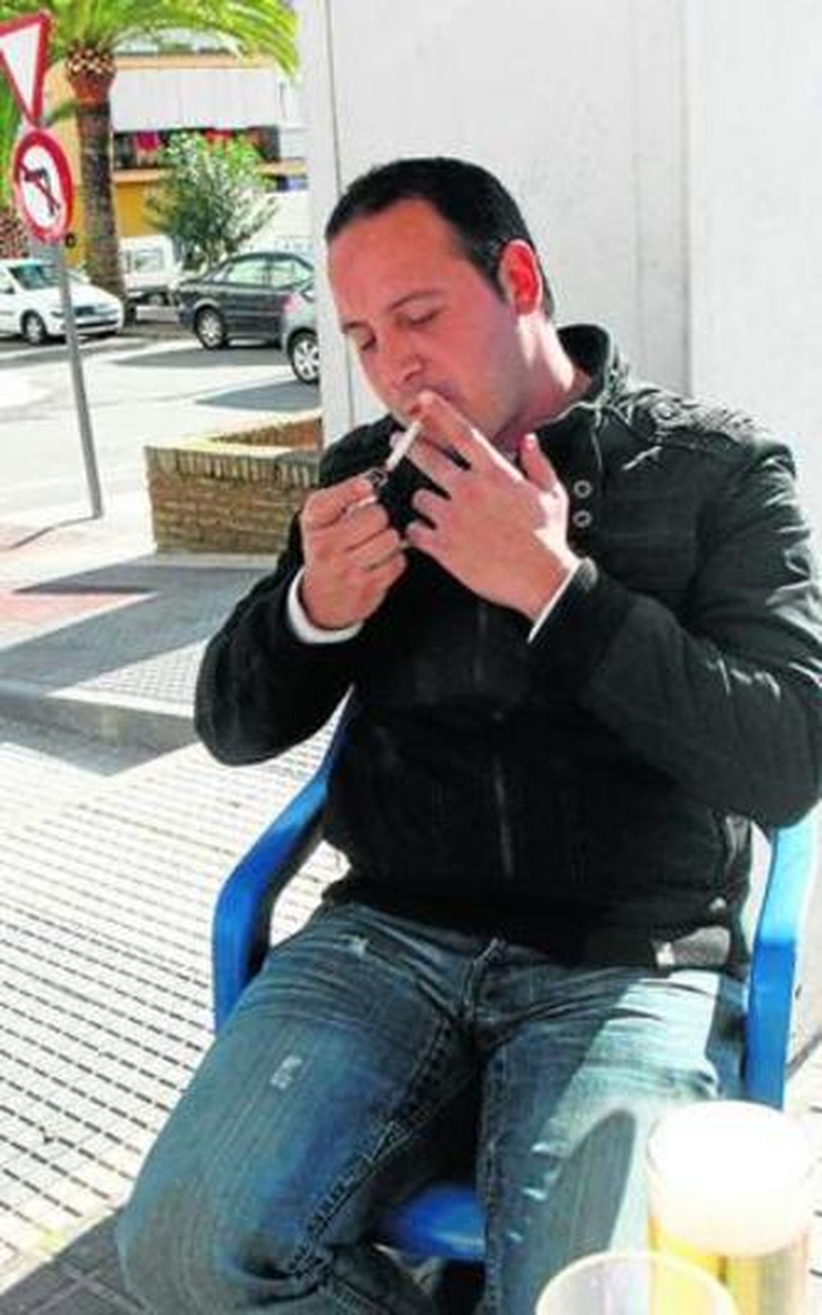 Un hombre se enciende un cigarro en el velador de un bar.