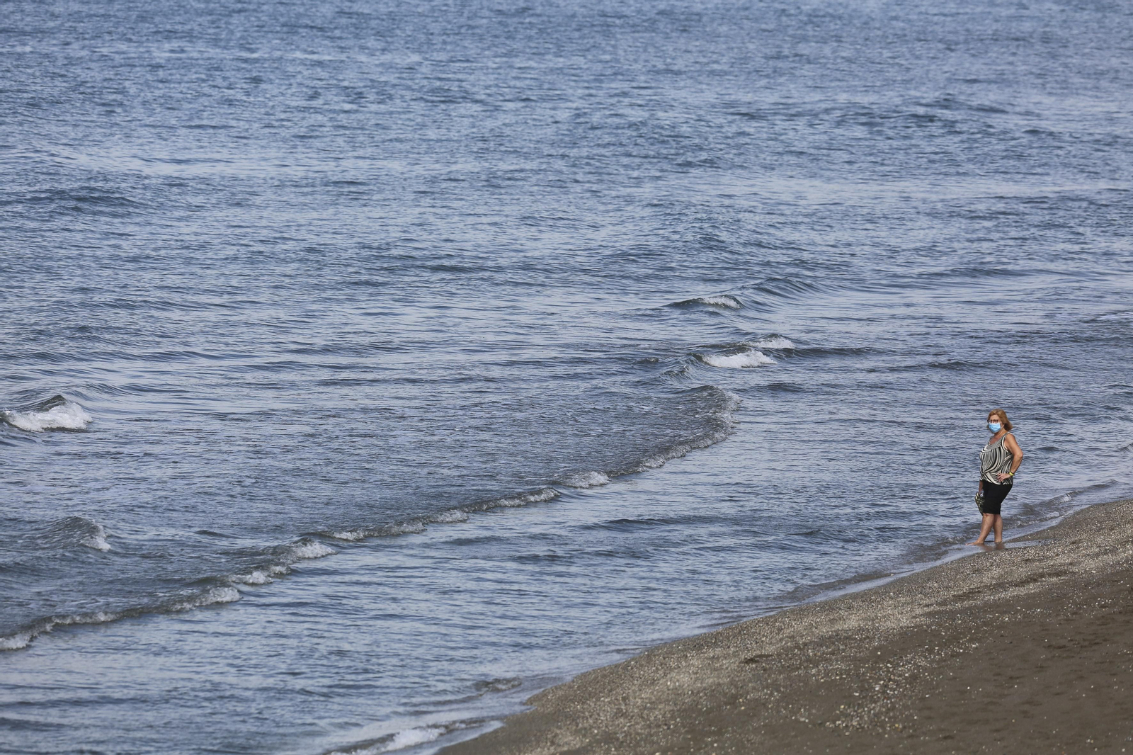 Una mujer se protege con una mascarilla en una playa en Málaga.