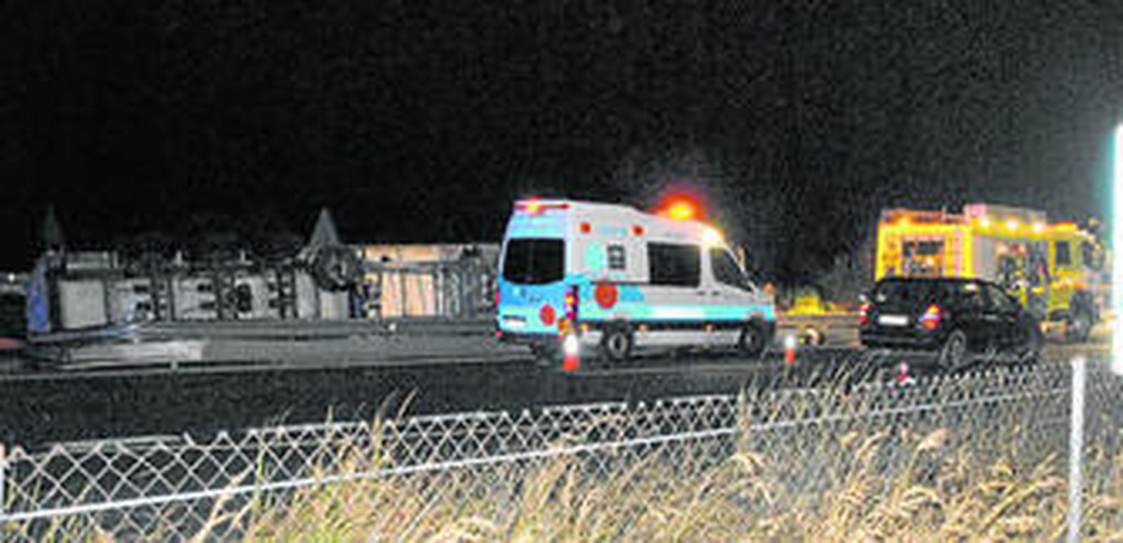 Personal sanitario y efectivos de bomberos, junto al trailer accidentado, que se aprecia volcado a la izquierda de la imagen.