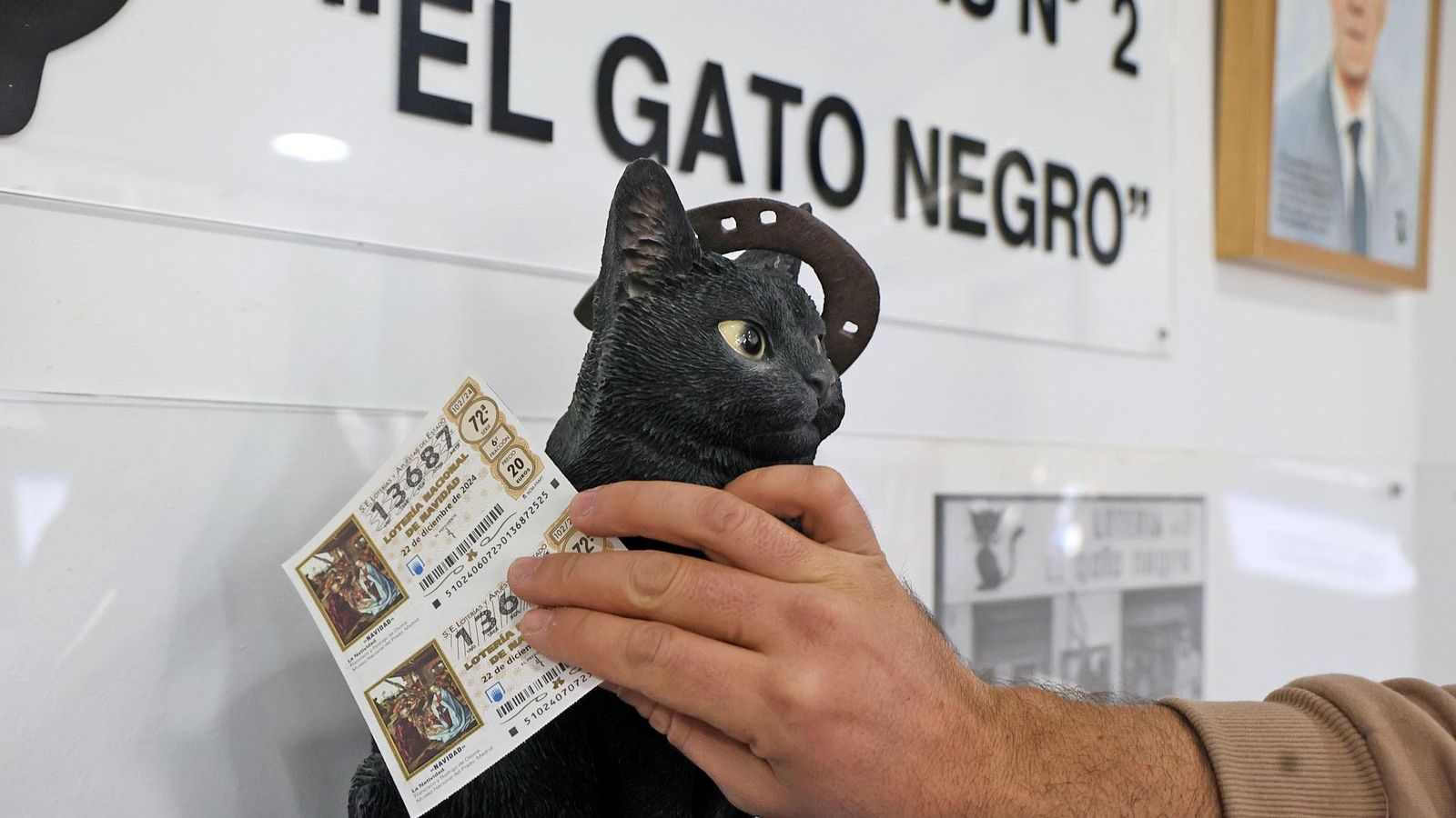 Una persona pasa su décimo por un gato negro en busca de que le de suerte.