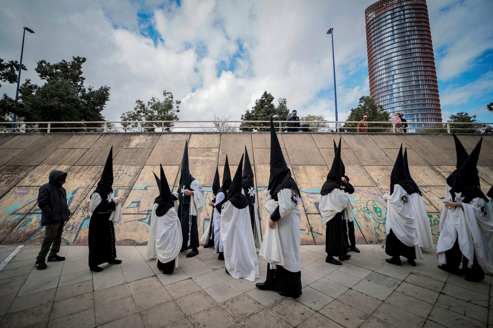 Nazarenos del Cachorro esperando y, de fondo, Torre Sevilla.