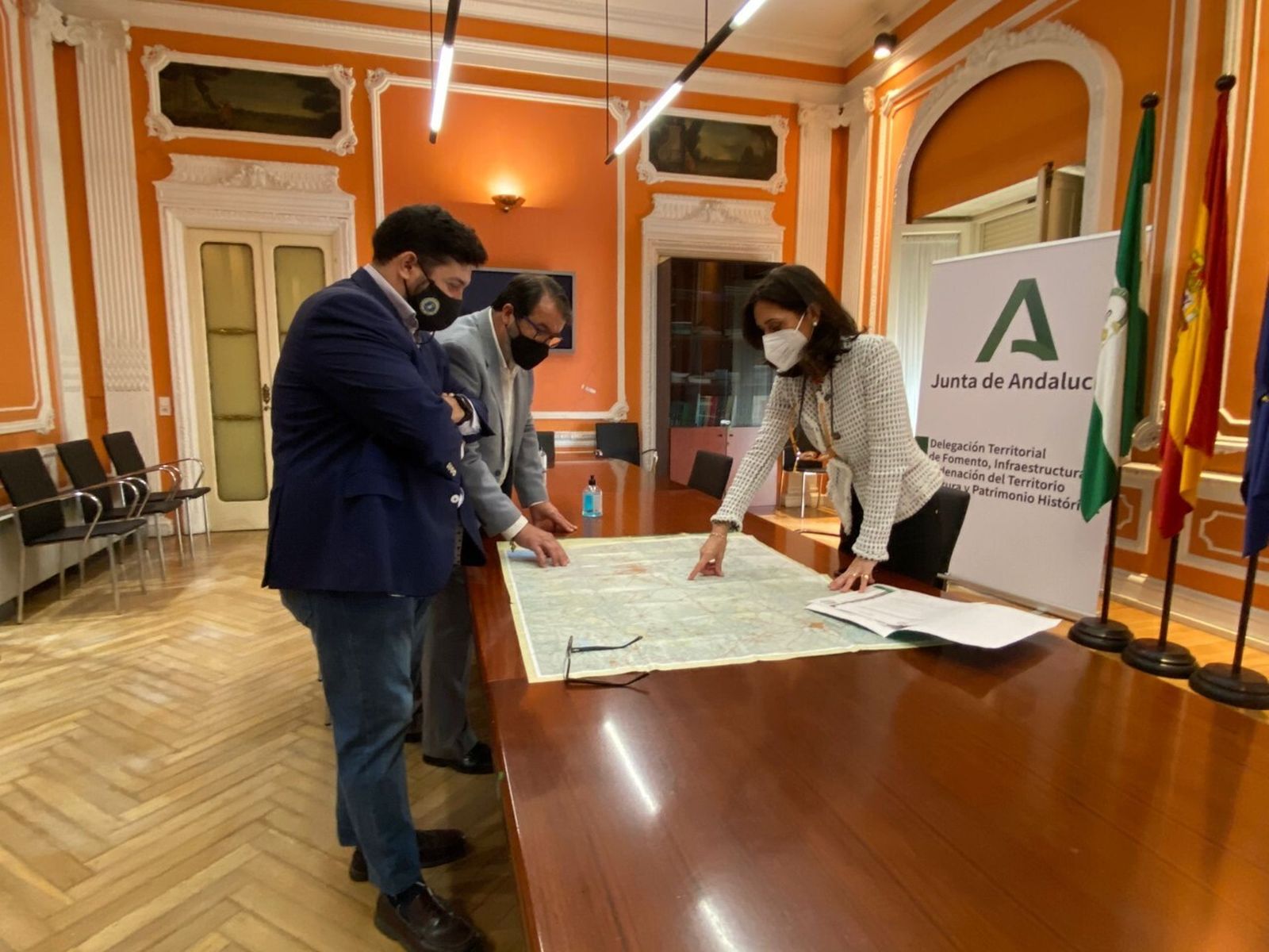 La delegada territorial de Fomento de la Junta, Susana Cayuelas, señala la carretera en un mapa junto a los alcaldes de Carmona y Lora del Río.