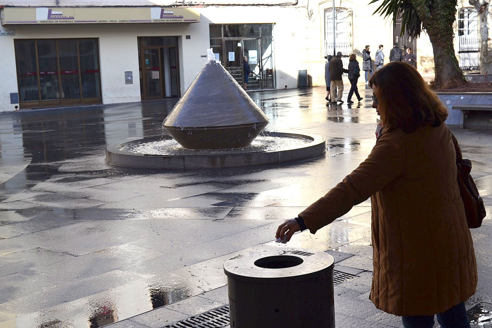 Una  mujer depositando basura en una papelera.