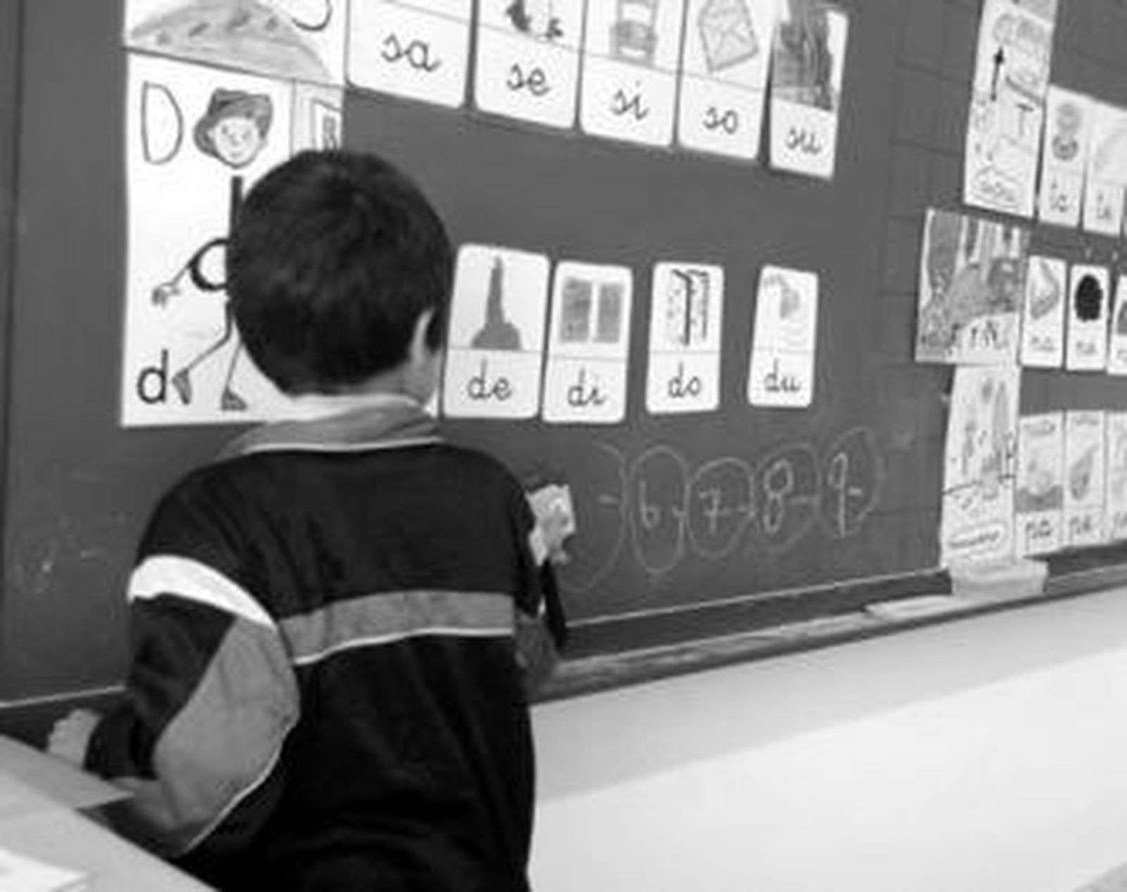 Un niño borra los dibujos de una pizarra en un colegio.