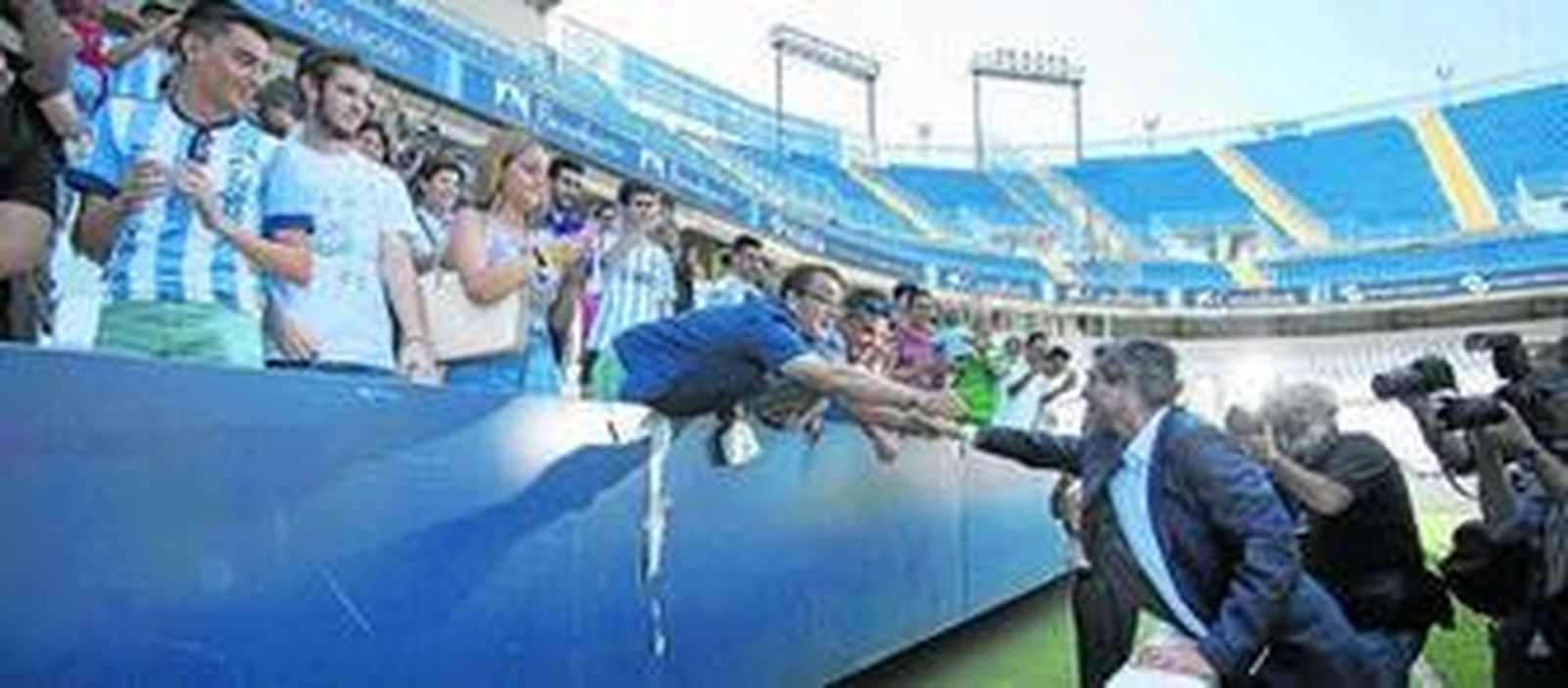 Juande Ramos se estira para darle la mano a un aficionado en la grada el día de su presentación como técnico del Málaga.
