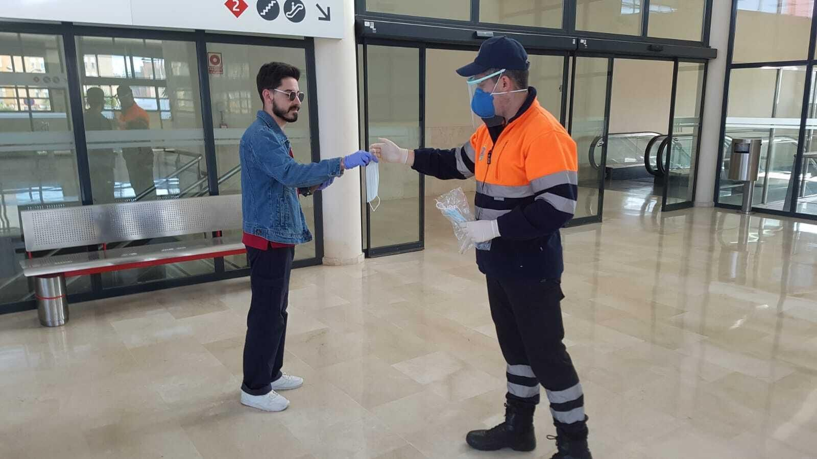 Un voluntario de Protección Civil entrega una mascarilla a un usuario de tren.