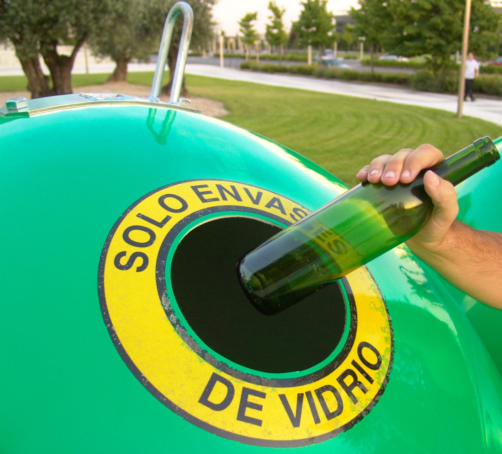 Una persona arroja una botella de vidrio a un contenedor.