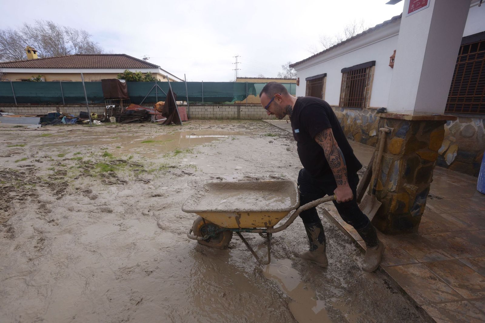 Un vecino de una parcela próxima al río Guadalquivir limpia el lodo acumulado en su vivienda