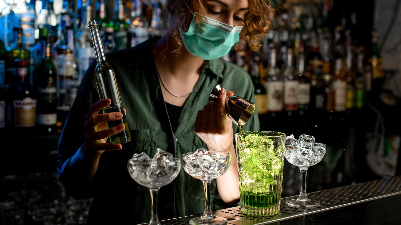 Una camarera, con mascarilla, preparando un cóctel.