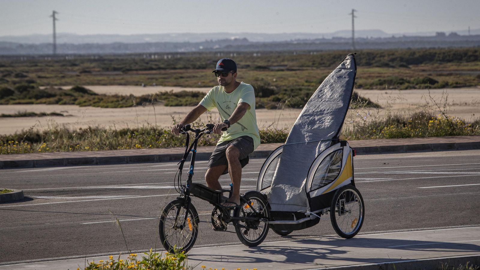 Un surfista con su tabla en un remolque para bicicletas. Un surfista con su tabla en un remolque para bicicletas.