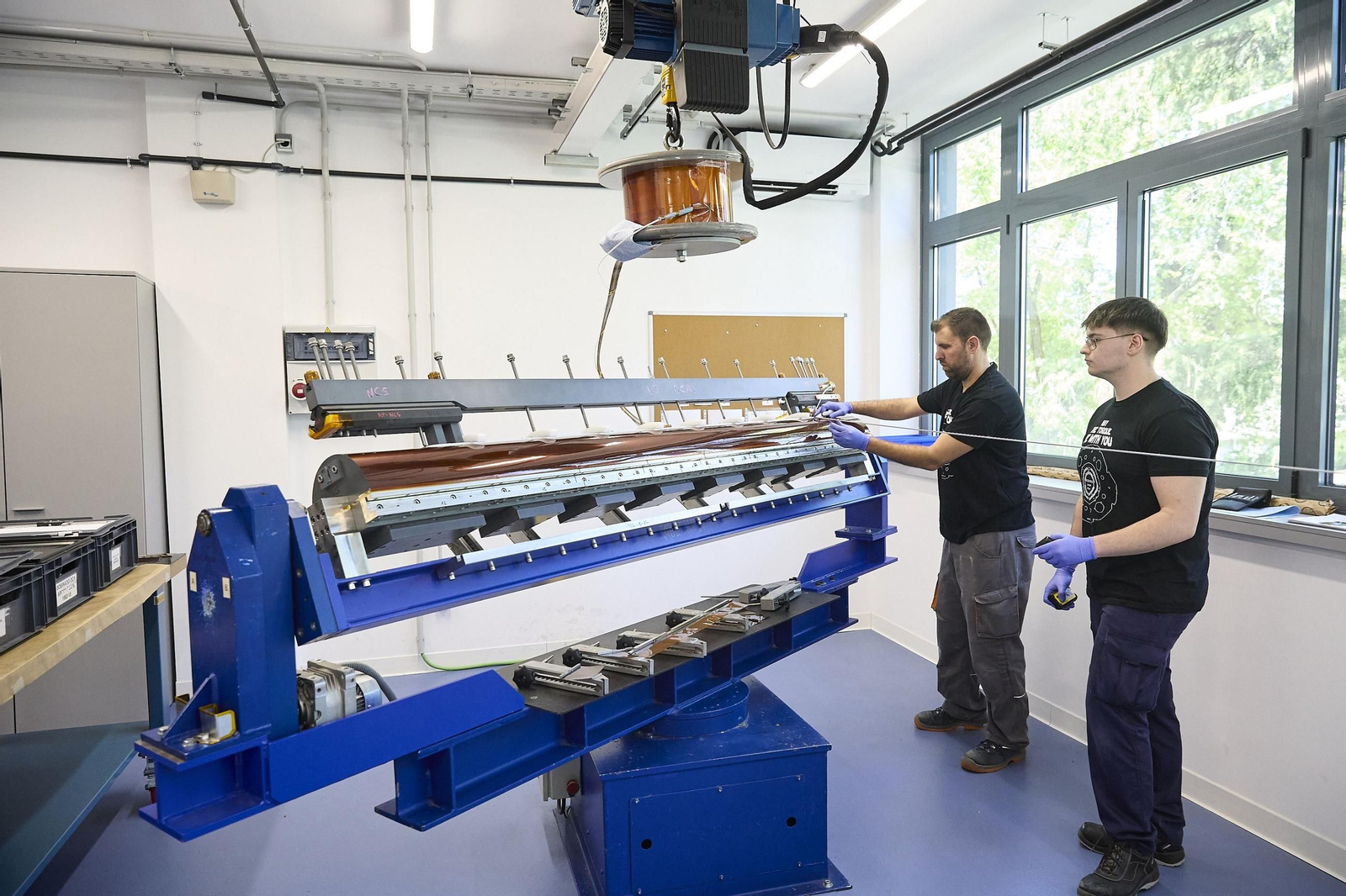 Dos trabajadores  manipulando maquinaria industrial y herramientas para el tratamiento y la producción de imanes y otros productos.