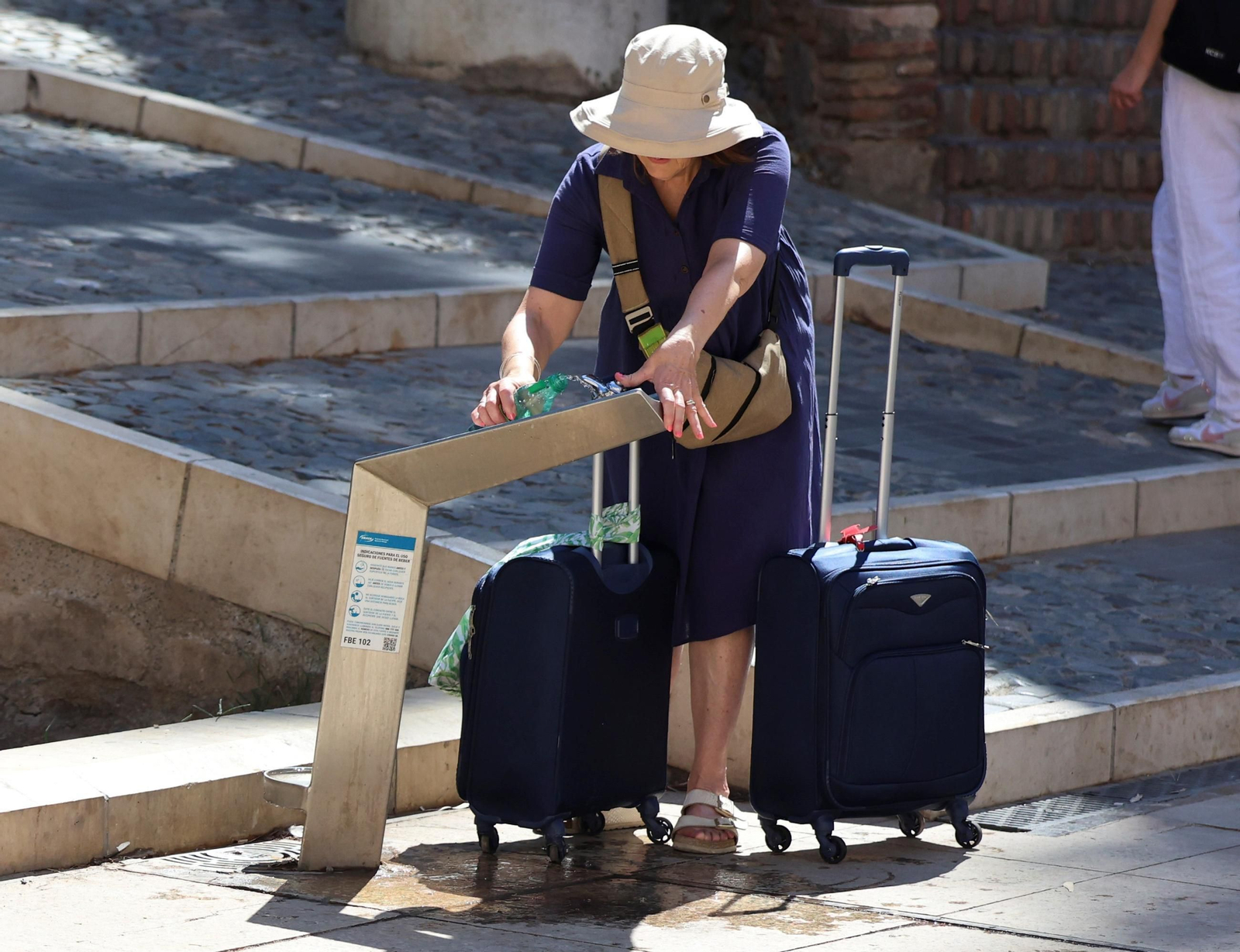 Una turista rellena una botella de agua en una fuente para sobrellevar el calor malagueño.