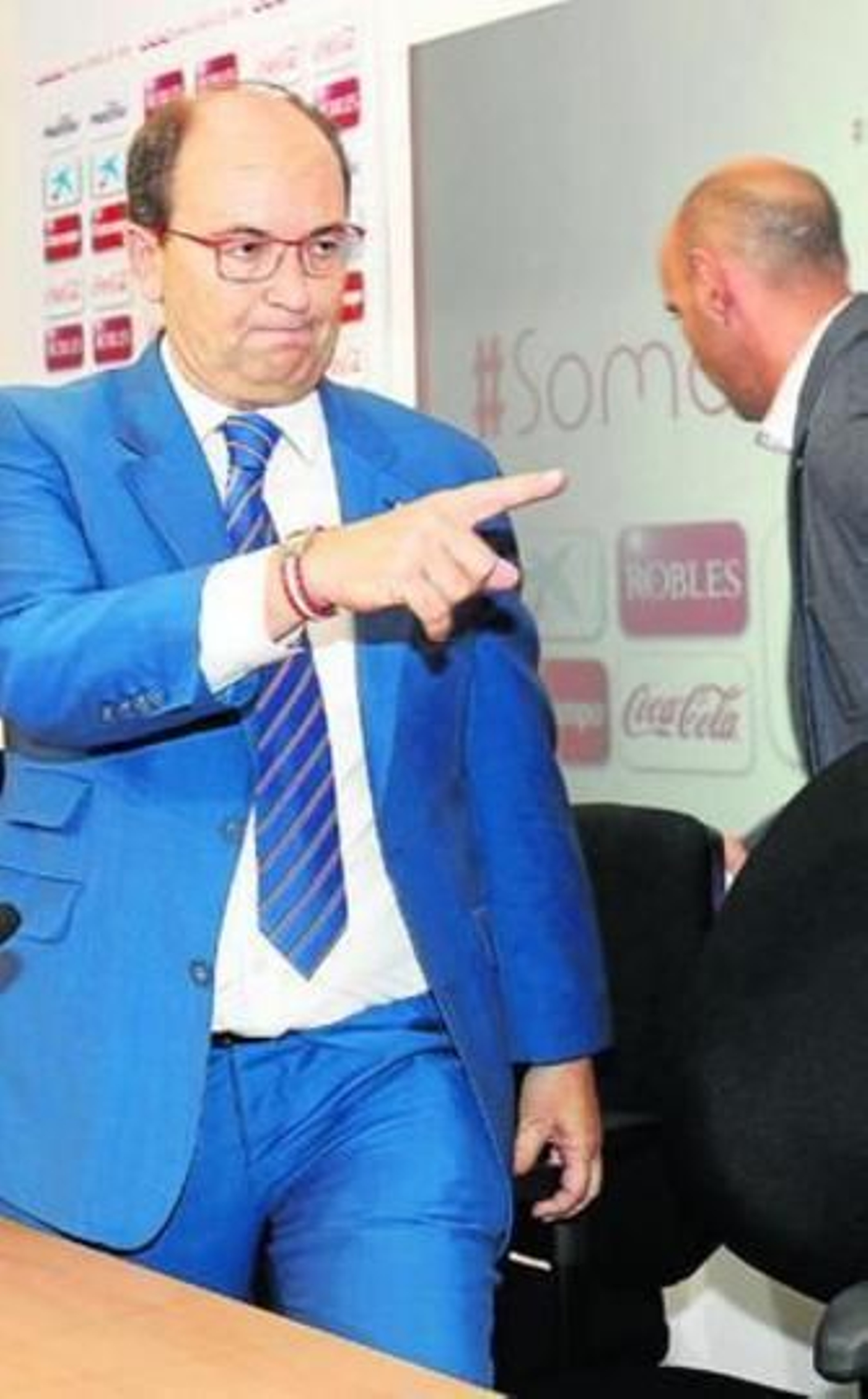 José Castro hace una indicación a alguien señalando con el dedo mientras Monchi pasa por detrás.