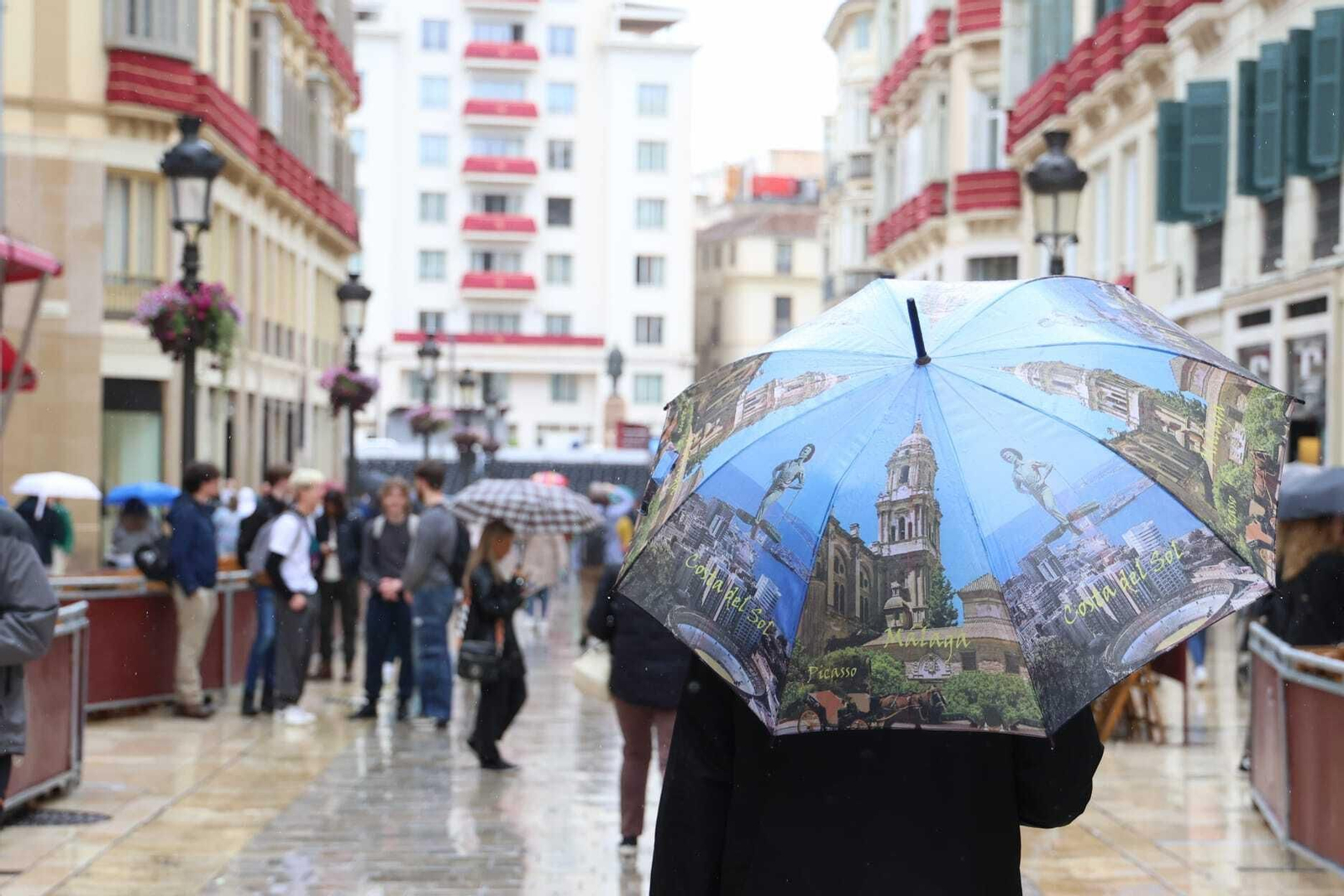 Una persona camina por la calle Larios con un paraguas con motivos malagueños.