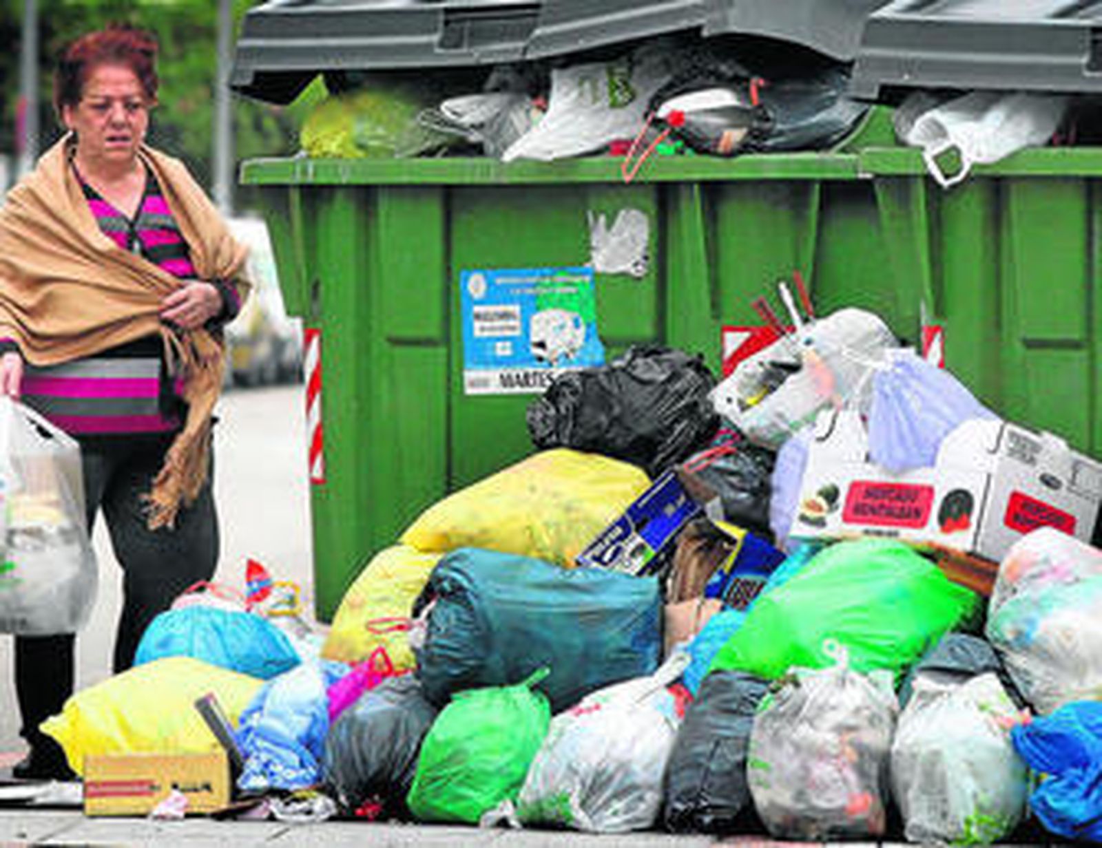 Una mujer tira la basura al suelo al estar llenos los contenedores.