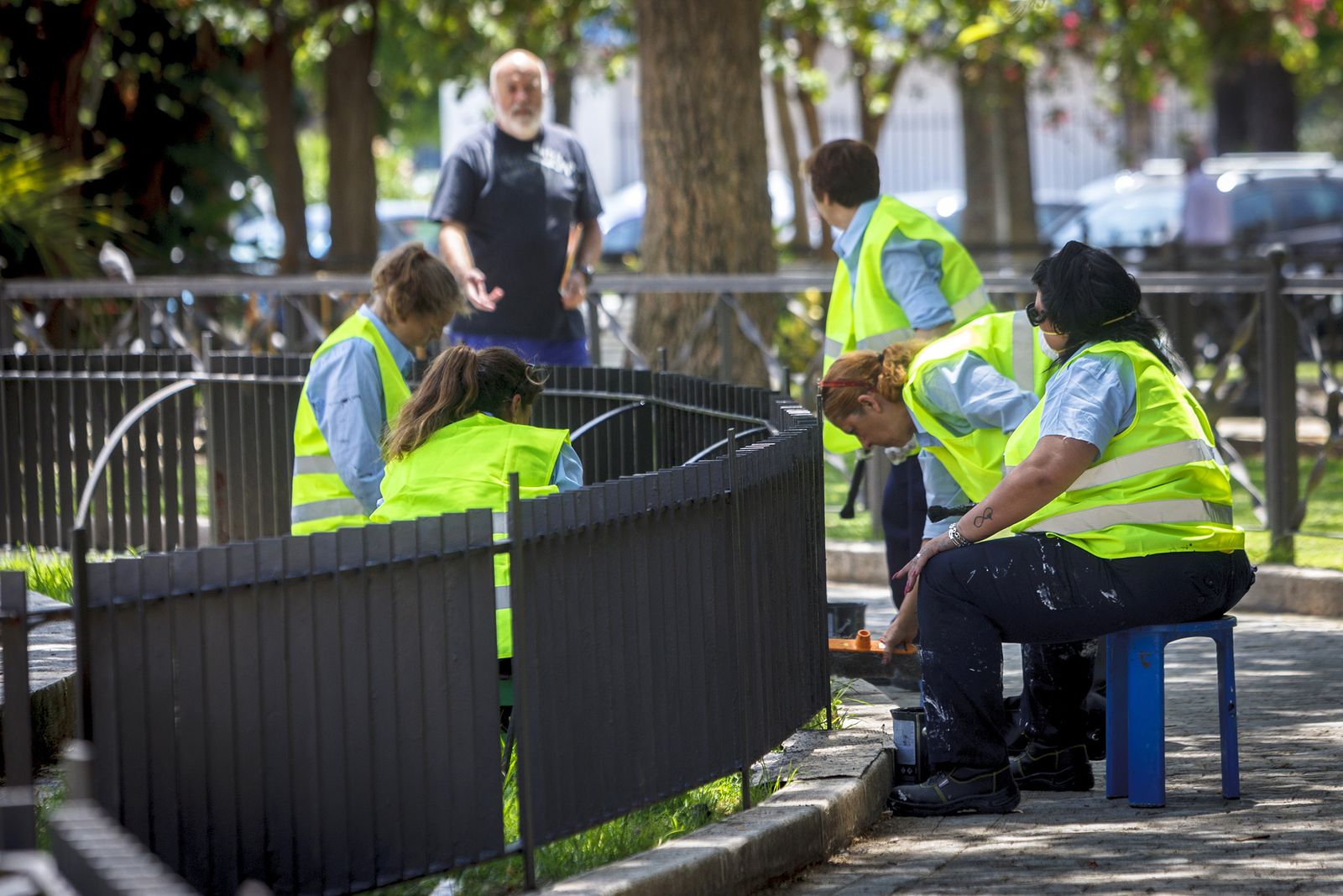 Personal que forma parte del plan de inclusión social trabaja en el pintado de una de las rejas de los jardines de la Plaza de España.