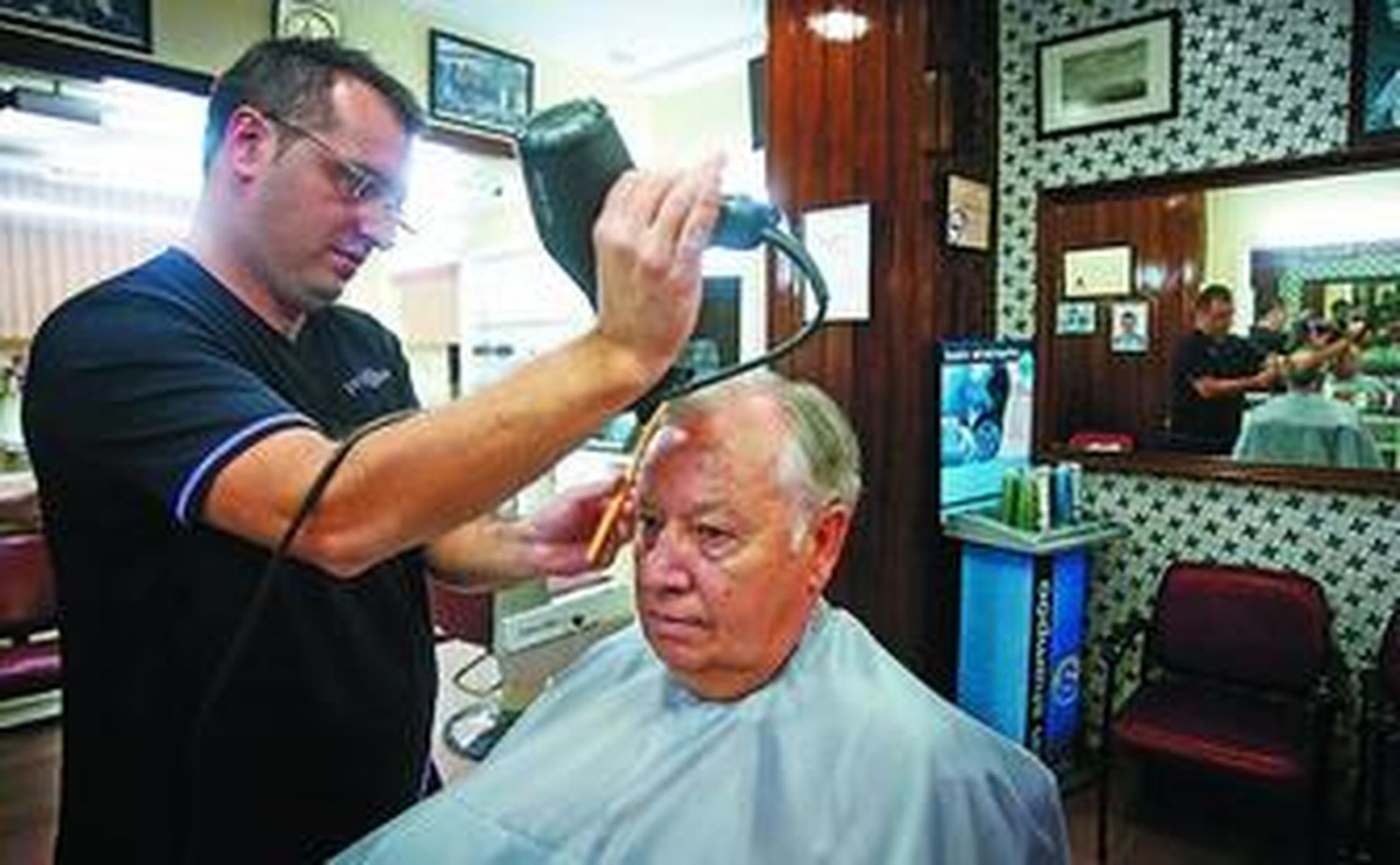 Juan Barroso peinando a su padre, que abandona el oficio después de cincuenta años con motivo de su jubilación.