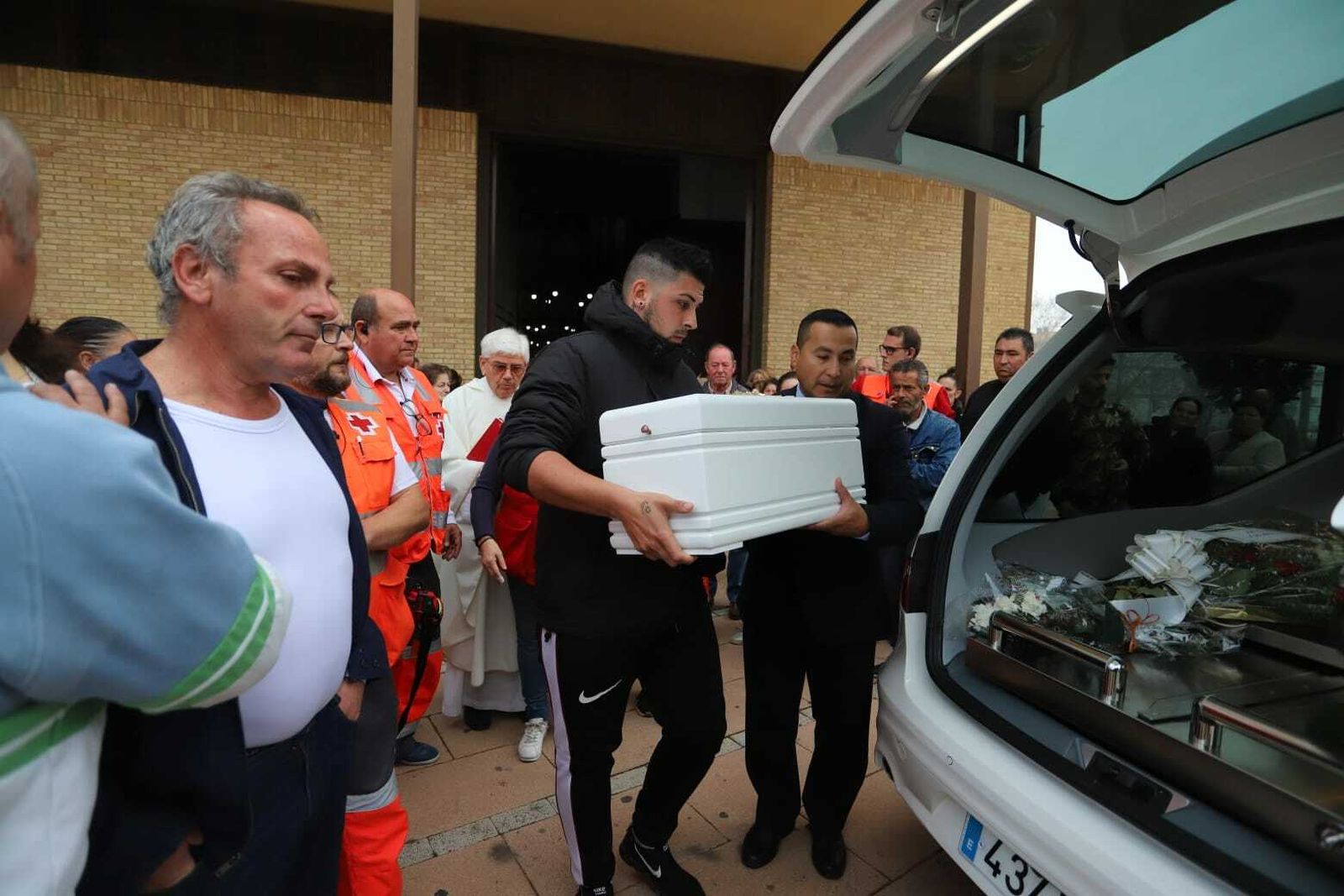 Un miembro de la familia introduce el féretro en el coche fúnebre en presencia del abuelo del menor, Paco Palma, en primer término.