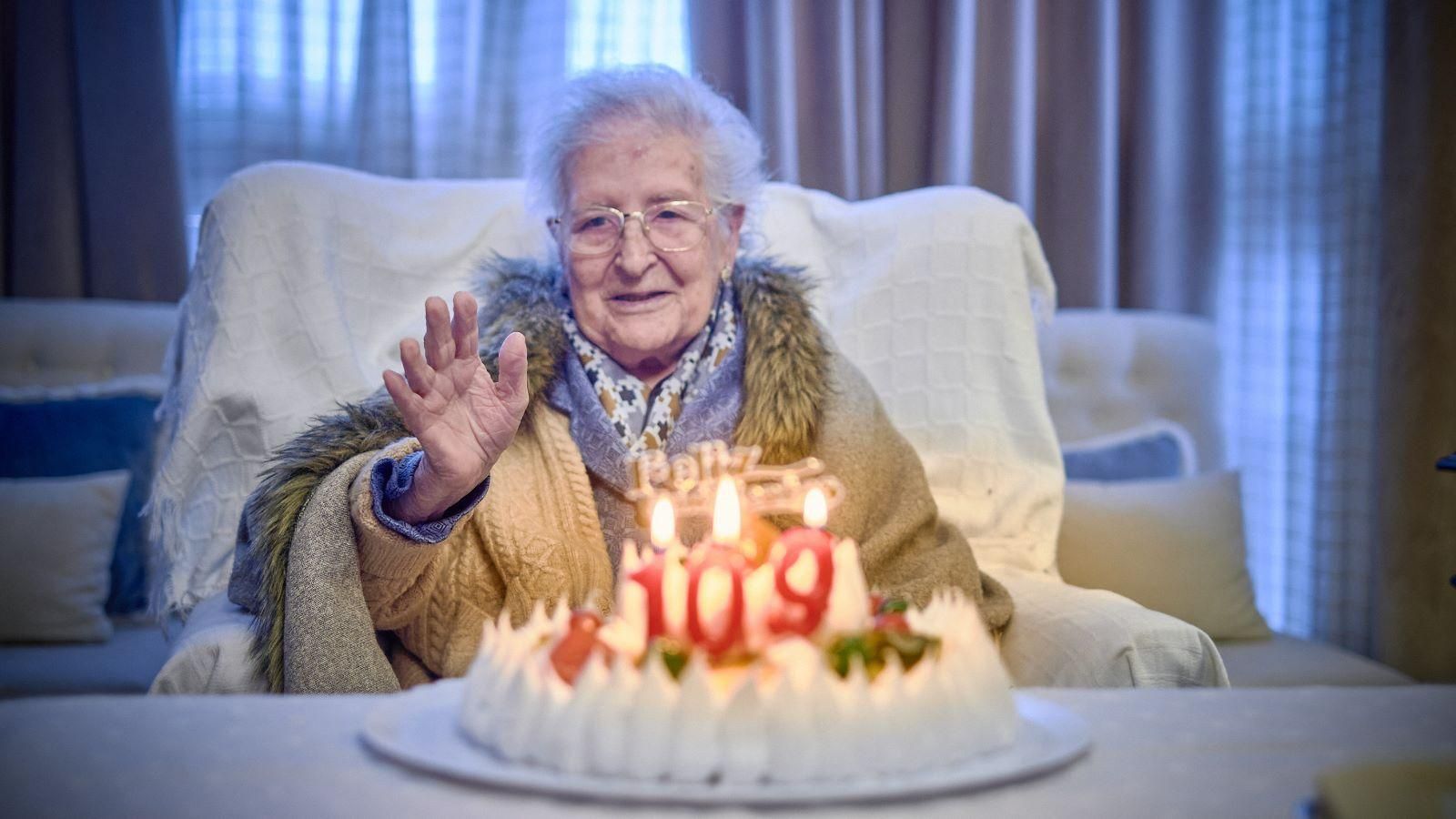 Ana María González saluda a la cámara con su tarta de cumpleaños delante.