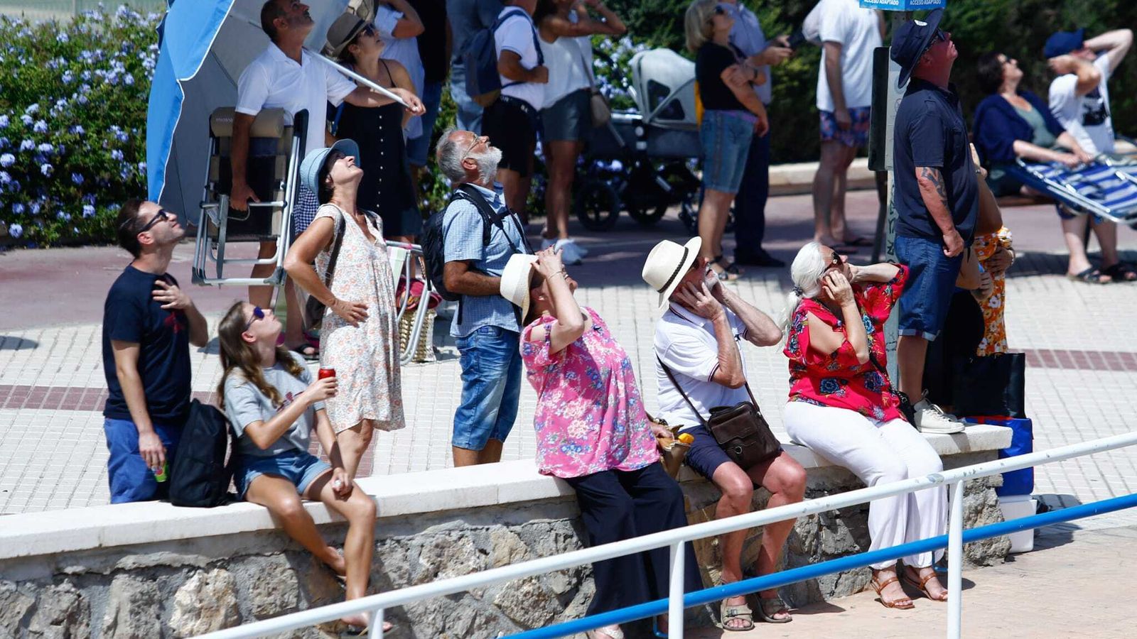 Varios asistentes miran al cielo y protegen sus oídos al paso de las aeronaves.