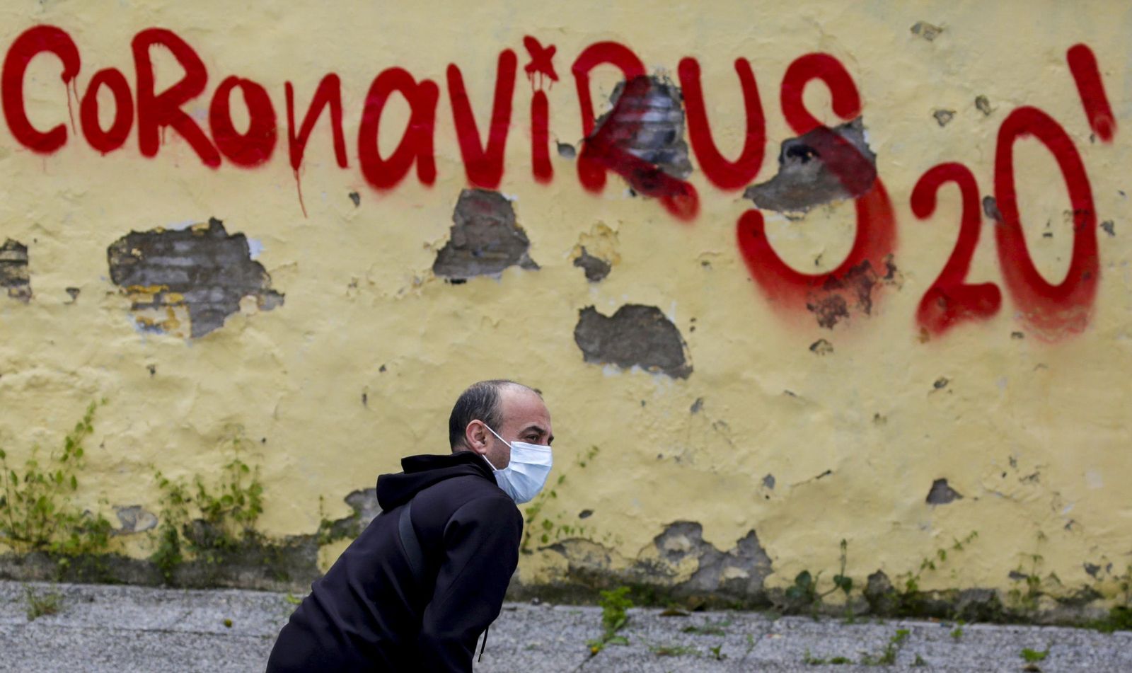 Un hombre en la calle pasa delante de una pared con un grafiti.