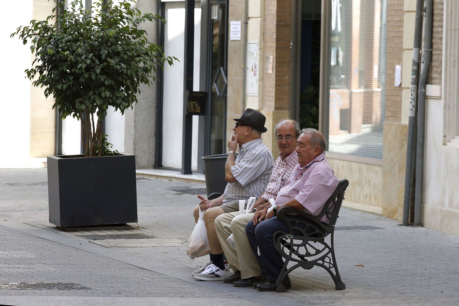 Tres hombres sentados en un banco de una de las calles de Huelva.