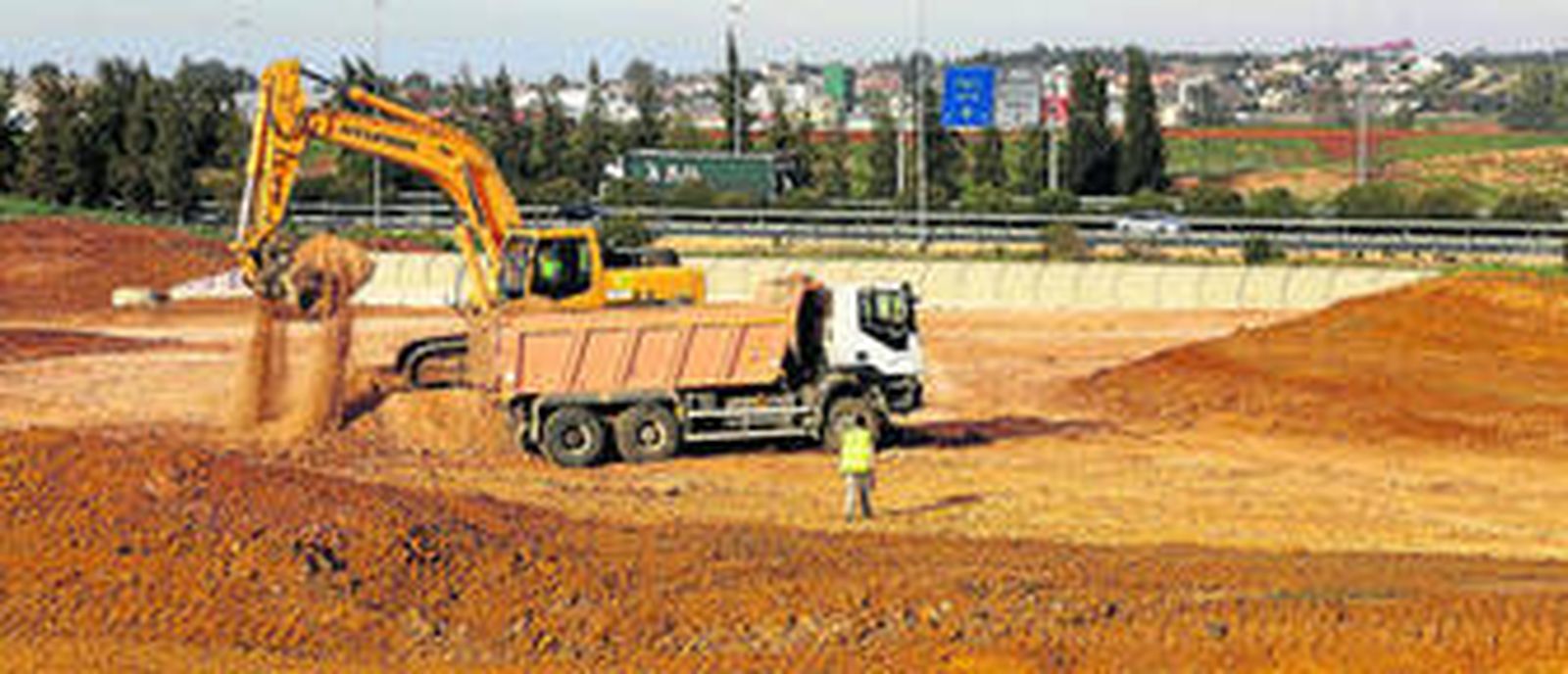 Un operario dirige los trabajos sobre el terreno para la SE-40 de un camión y otra maquinaria pesada, junto a la autopista a Cádiz (A-4).
