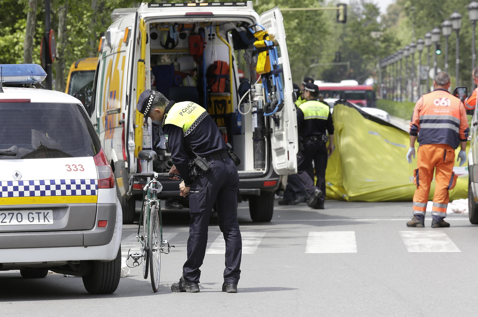 Un agente de la Policía Local recoge la bicicleta de un herido, con los técnicos del 061 al fondo.