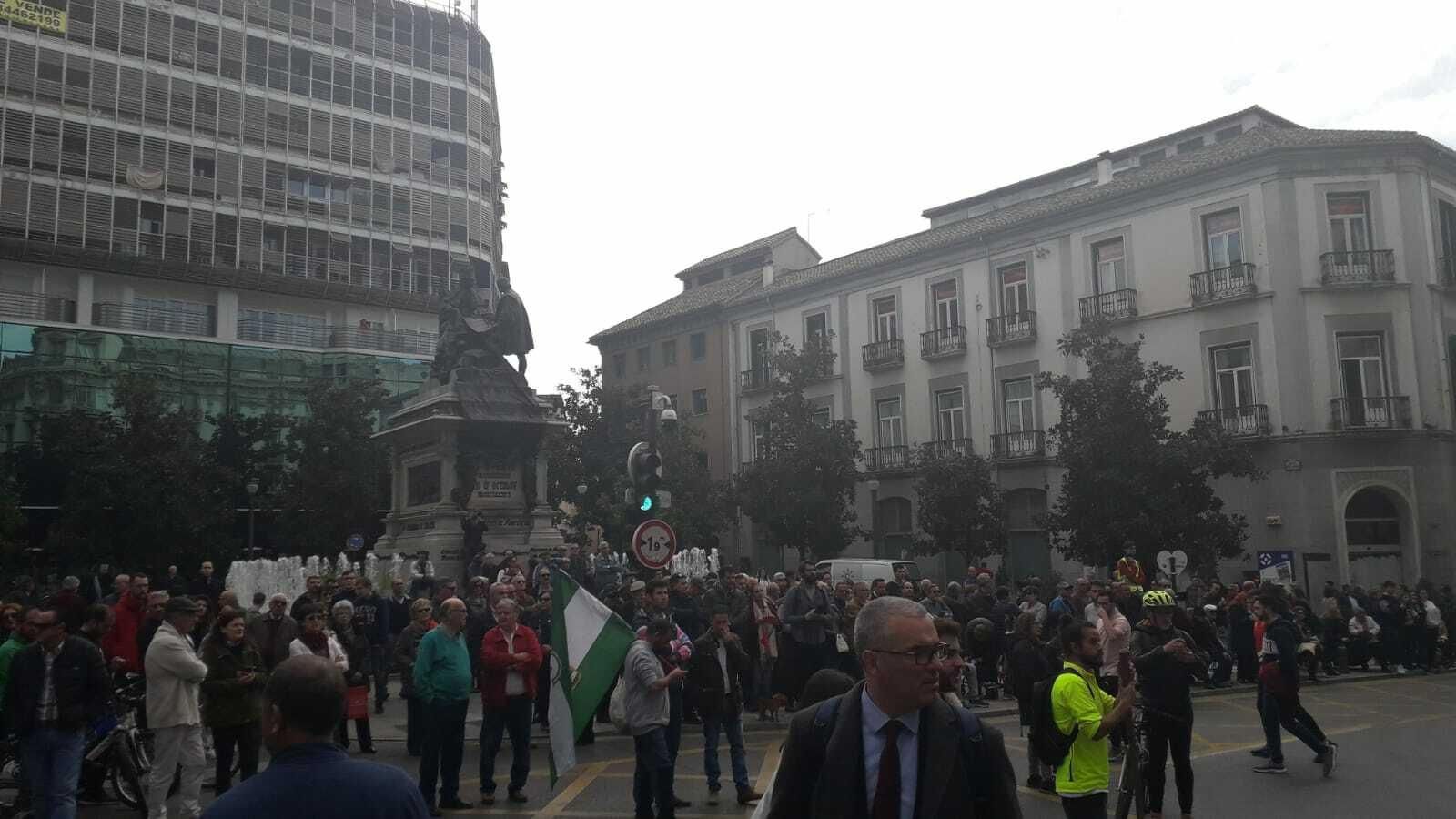 Personas aguardan la llegada de la manifestación junto a la estatua de Isabel La Católica.
