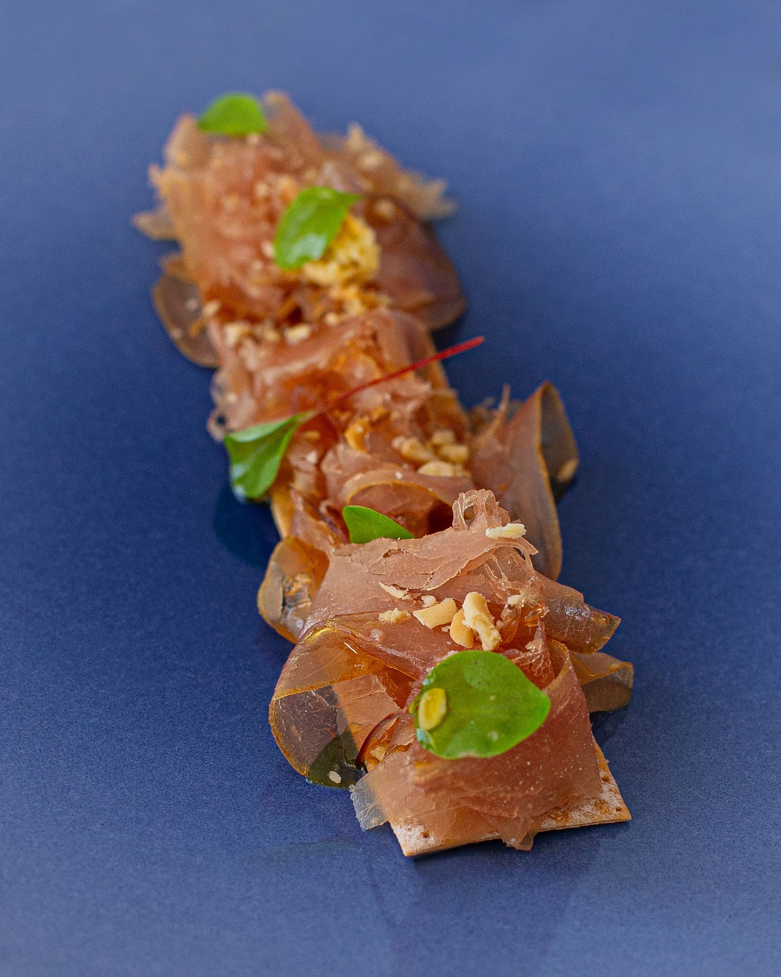 Mojama sobre crujiente de pan aderezado con piñones y aceite de oliva