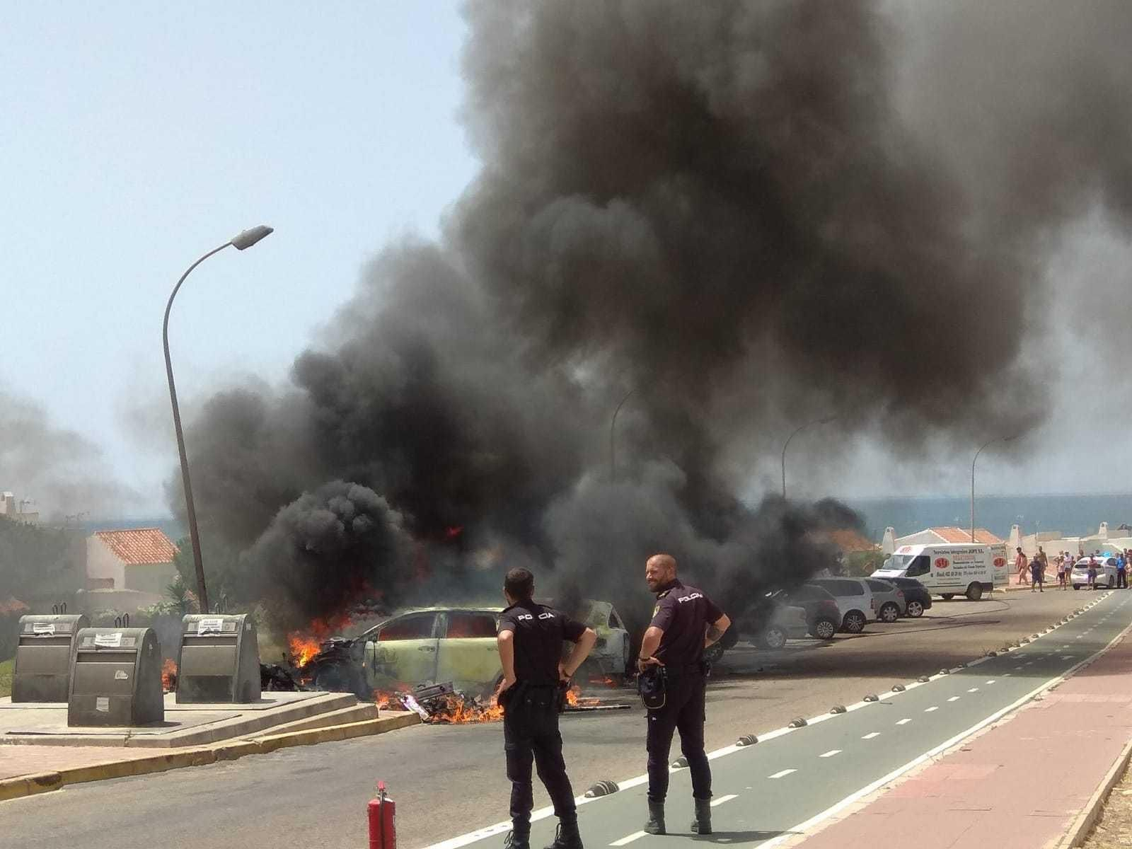 Dos agentes de la Policía local presencian la quema de vehículos.