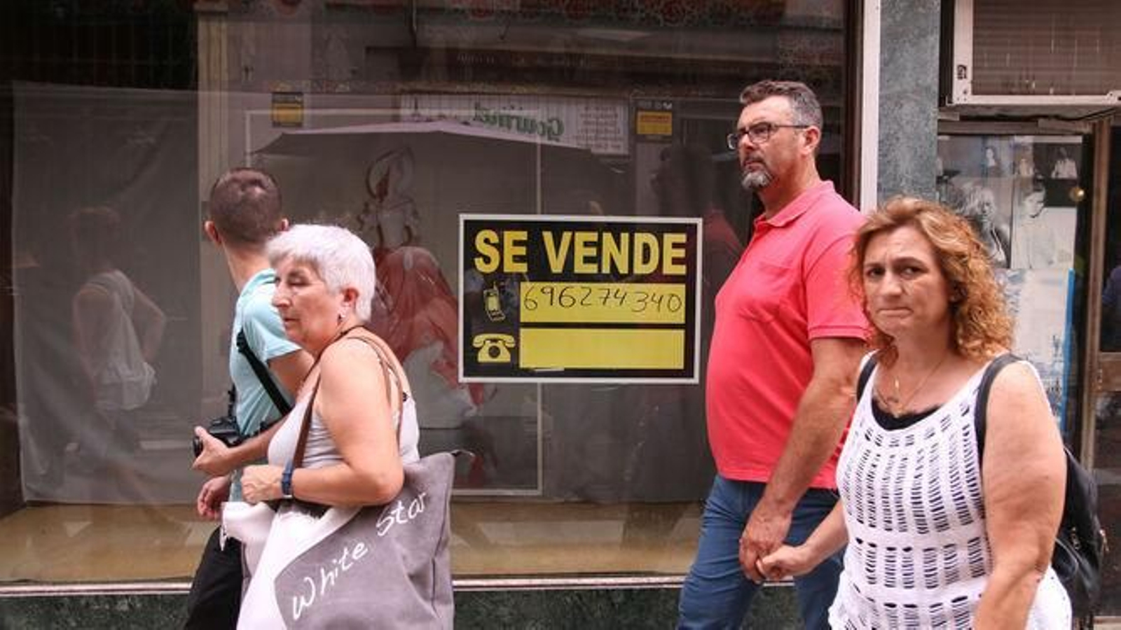 Transeúntes junto a un cartel de 'se vende' en la Calle de las Tiendas.