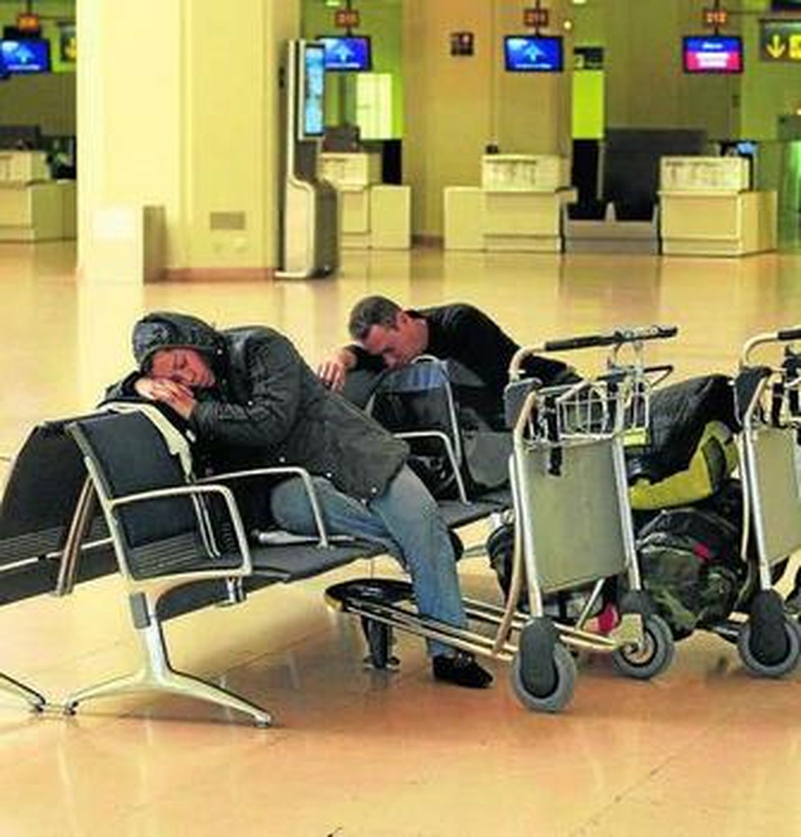 Dos viajeros echan una cabezada en los bancos del aeropuerto.